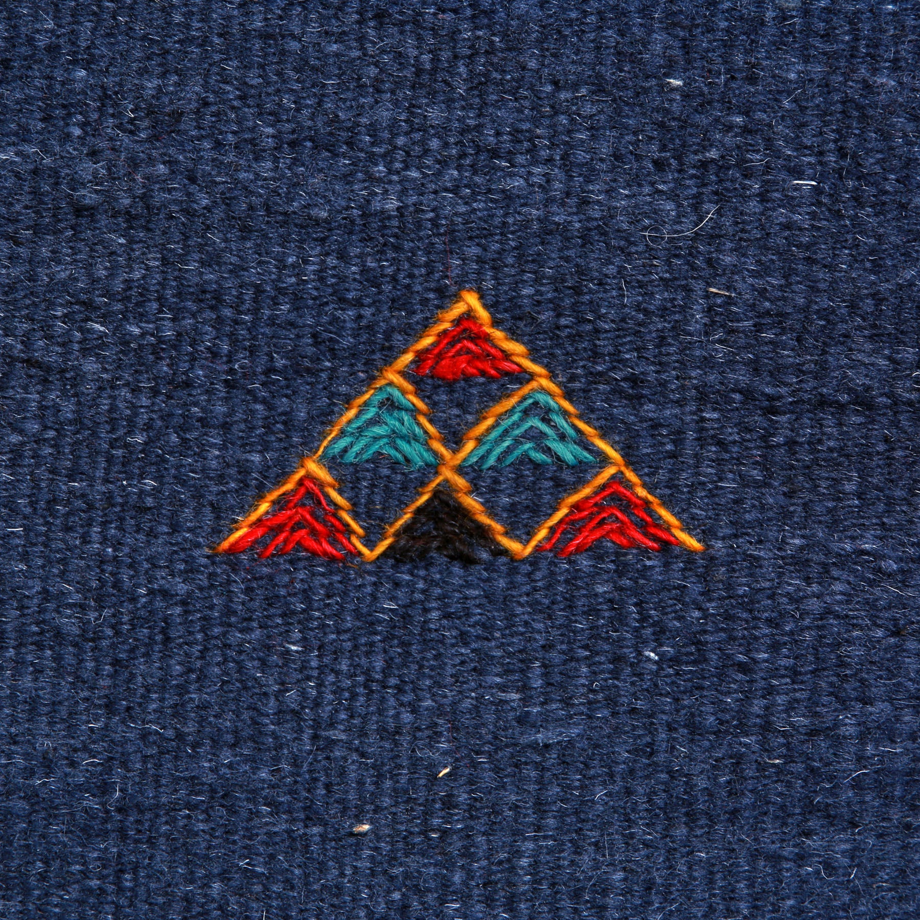 dettaglio di un simbolo amazigh a forma di piramide ricamato su un tappeto artigianale marocchino a tessitura piatta blu