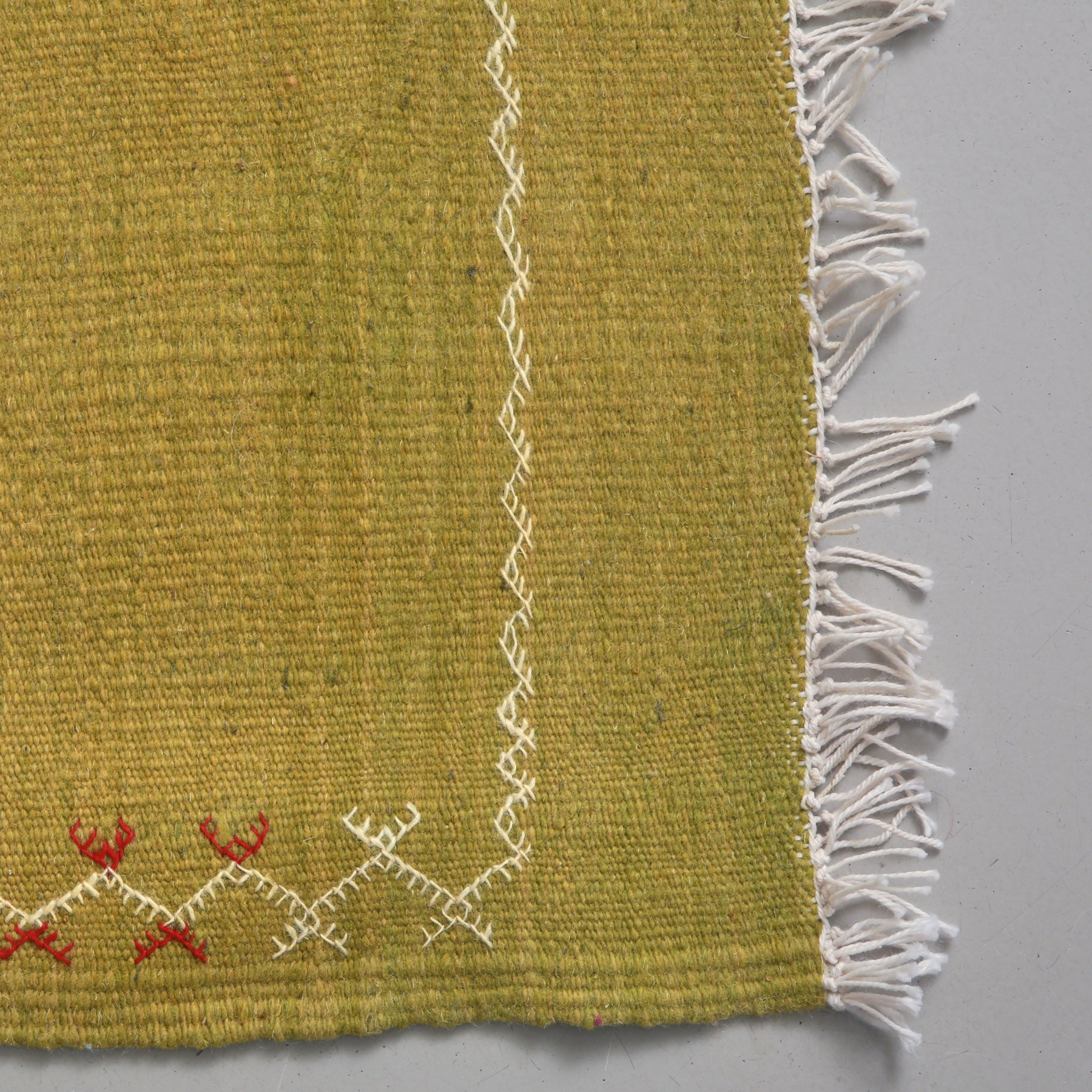 dettaglio dell'angolo e della cornice ricamata in bianco di un tappeto marocchino akhnif a tessitura piatta verde