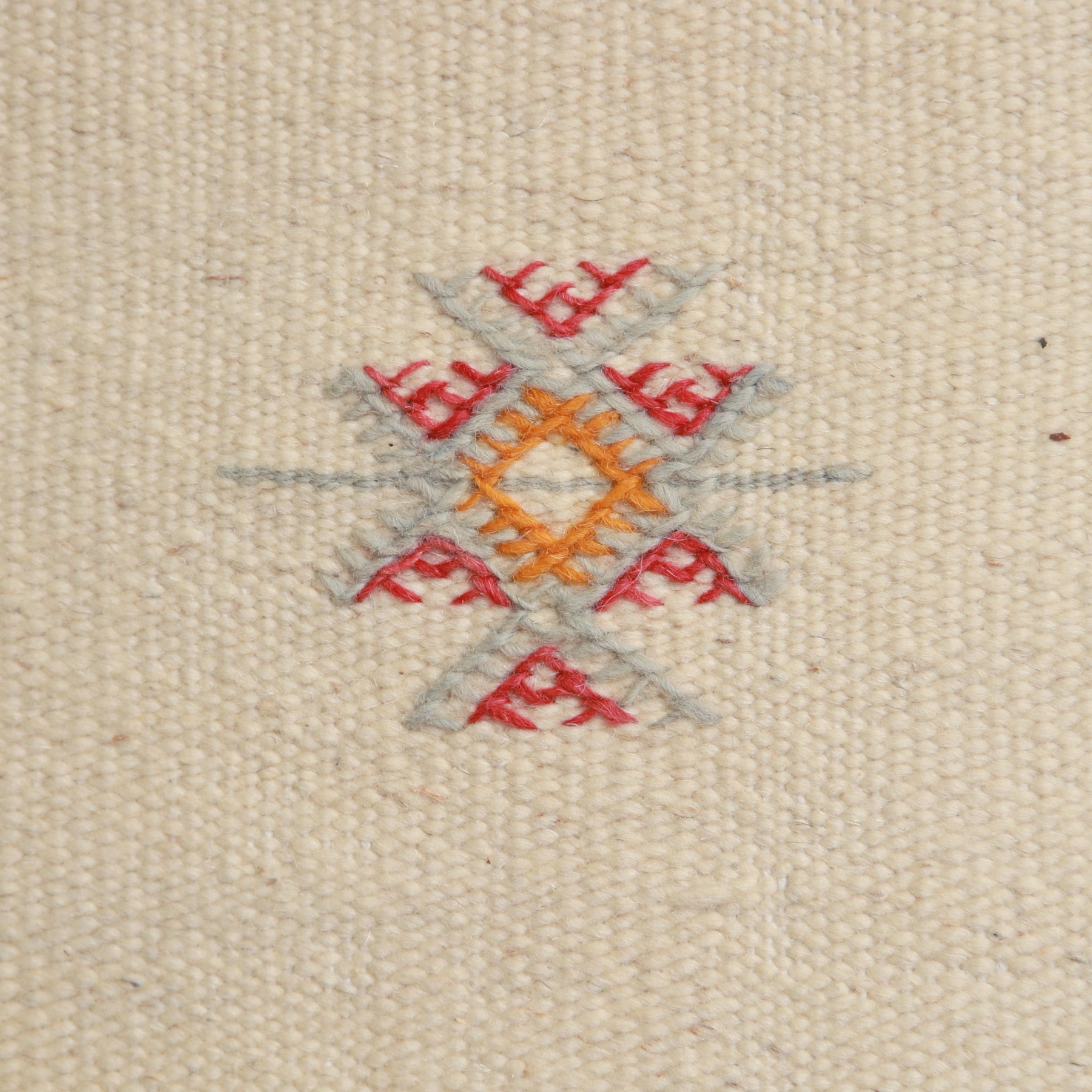 dettaglio di un simbolo amazigh ricamato in grigio rosso e arancione su un tappeto marocchino akhnif a tessitura bianca in lana bianca