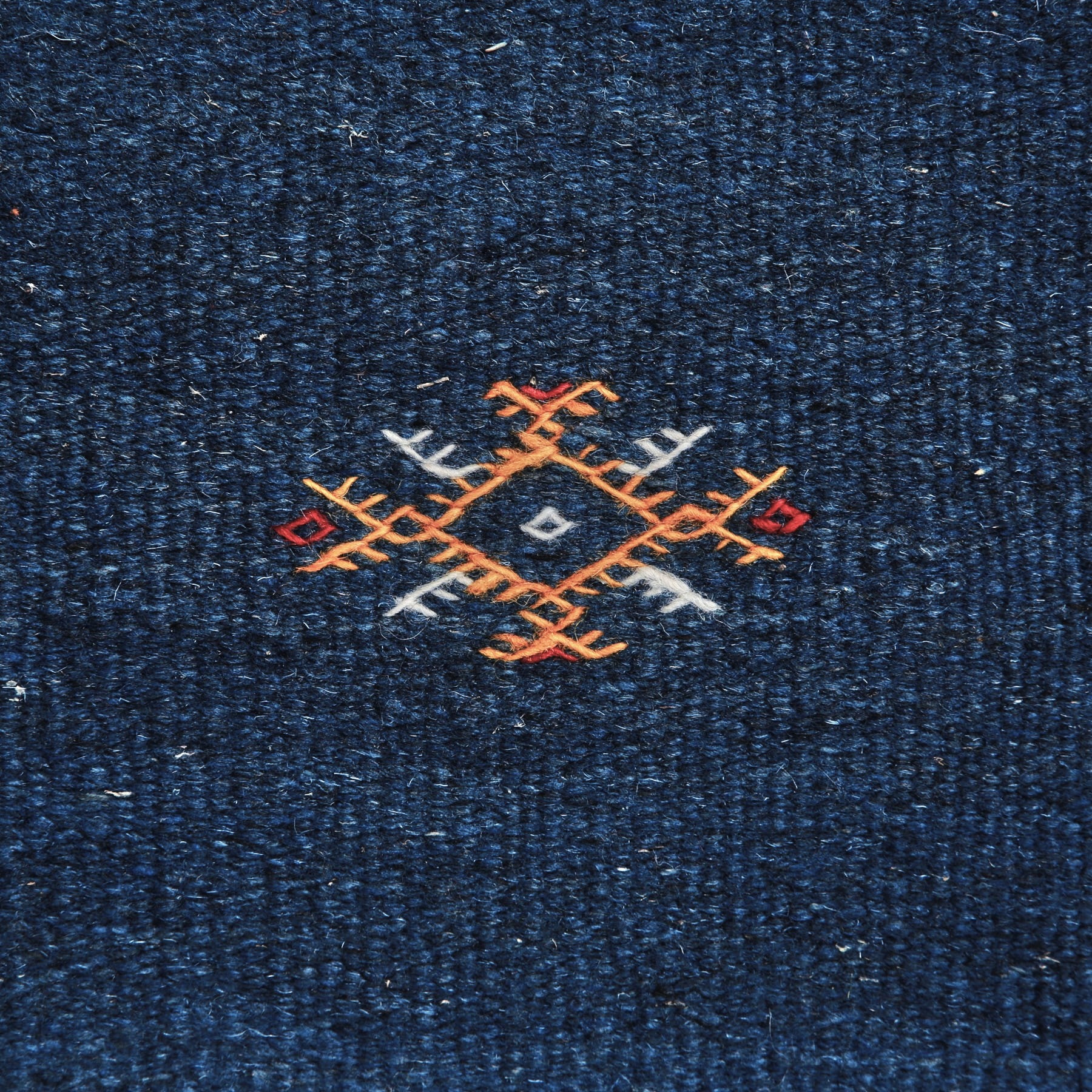 dettaglio di un simbolo amazigh ricamato in arancione bianco e rosso su un Tappeto marocchino akhnif a tessitura piatta blu