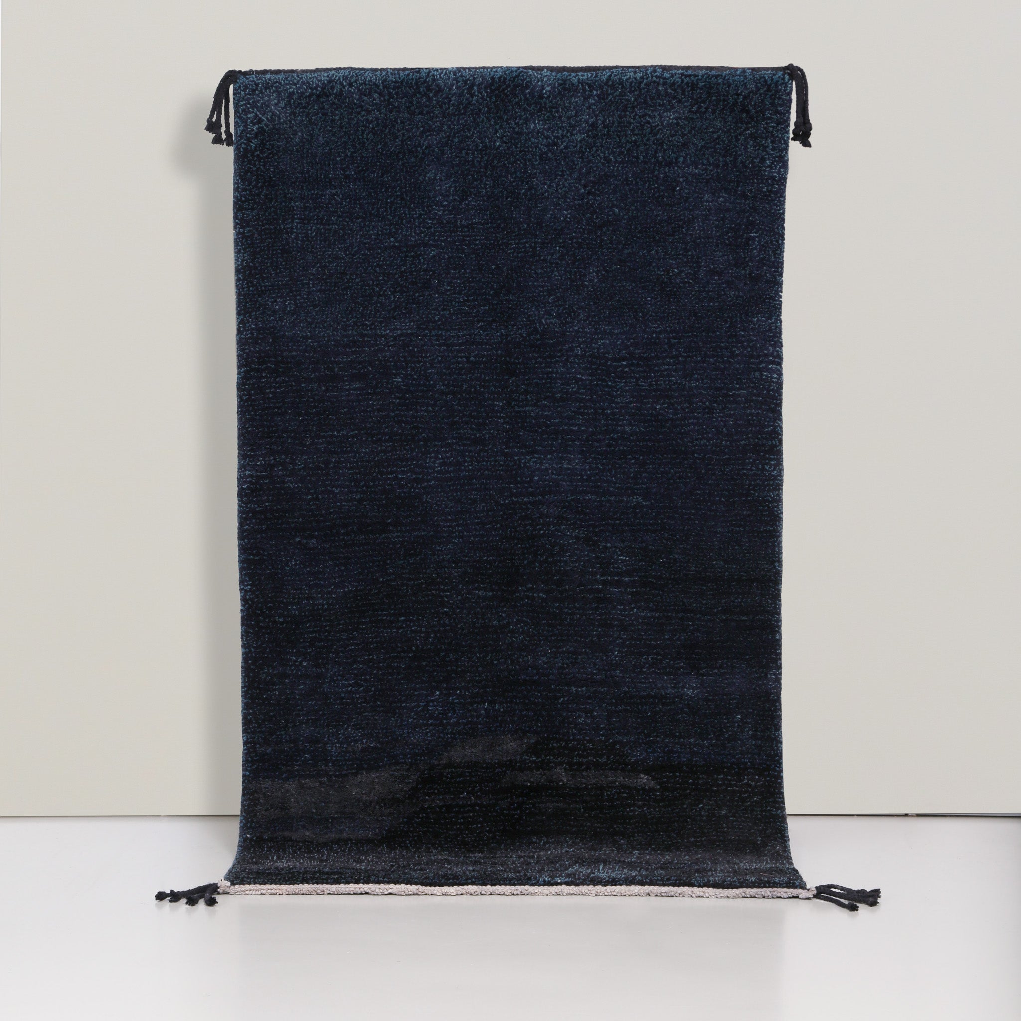 Tappeto berbero marocchino Beni Mrirt con sfumature blu scuro, annodato a mano, con frange nere, mostrato intero su sfondo chiaro.