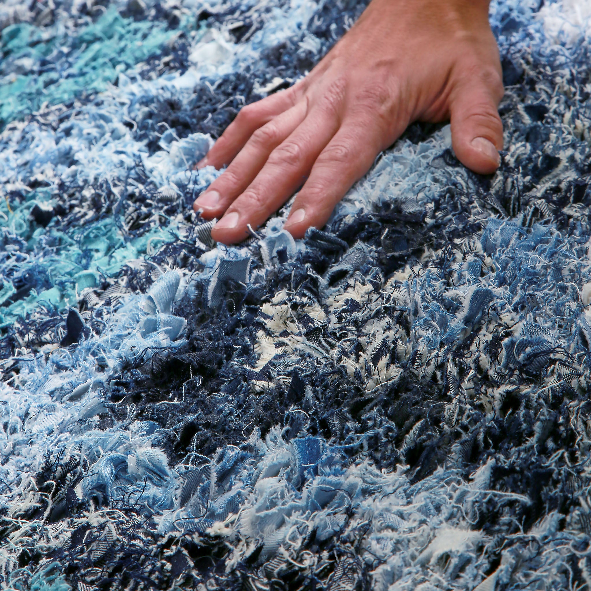 mano appoggiata su un tappeto realizzato annodando fettuccine di tessuto ricavate da vecchi jeans