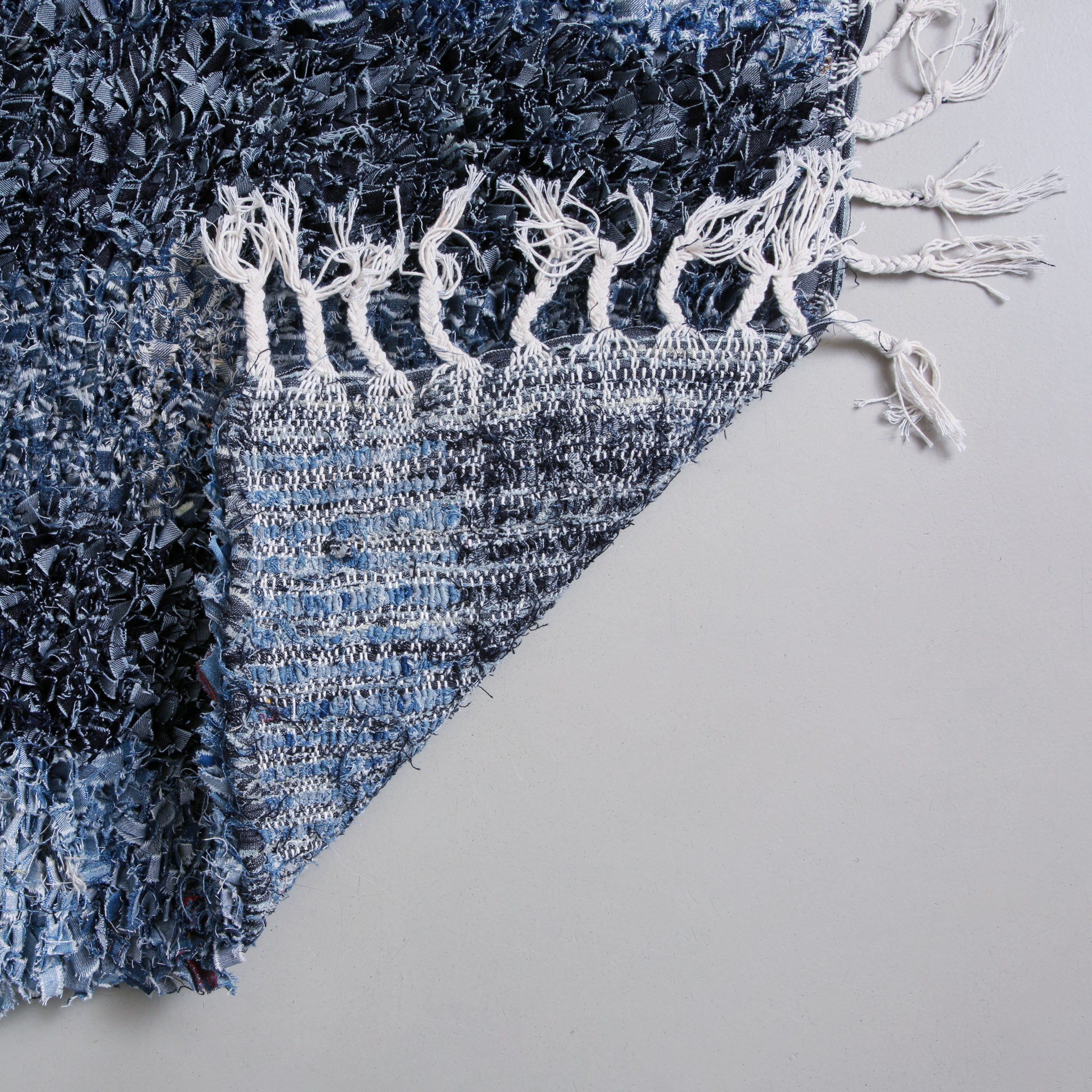 retro dell'angolo di un angolo di un tappeto realizzato con jeans di diverso colore e con la frangia in cotone bianco