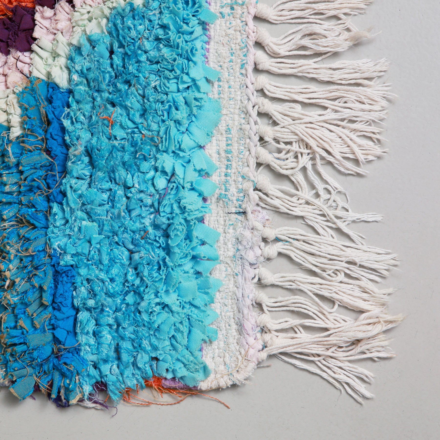 angolo di un tappeto boucherouite con frangia bianca e stracci di tessuti azzurri