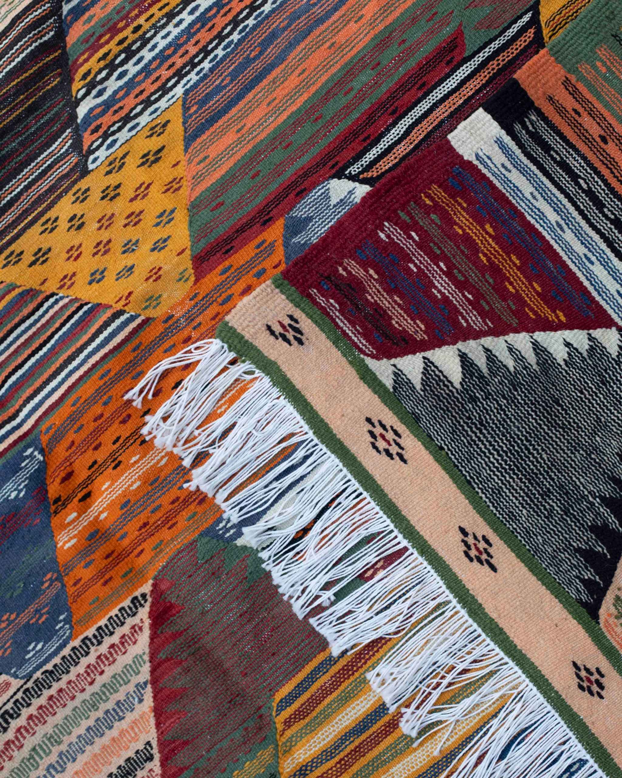 Dettaglio kilim marocchino Kharita: micro-pattern geometrici a righe e punti nella tessitura piatta in lana multicolore, con frange su un lato.
