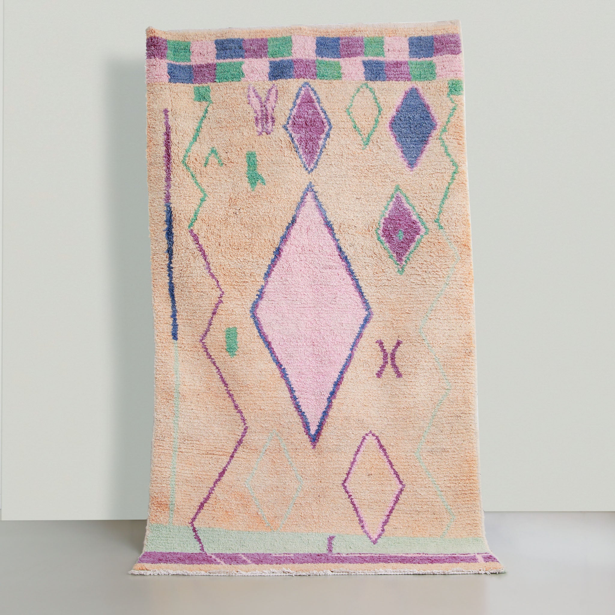 tappeto marocchino bujaad in lana rosa pastello con un grande rombo centrale rosa acceso con cornice blu e viola e altri 4 rombi di cui due viola uno ble e uno rosa, ci sono due righe a zigzag ai lati viola e verdi e azzurro pastello