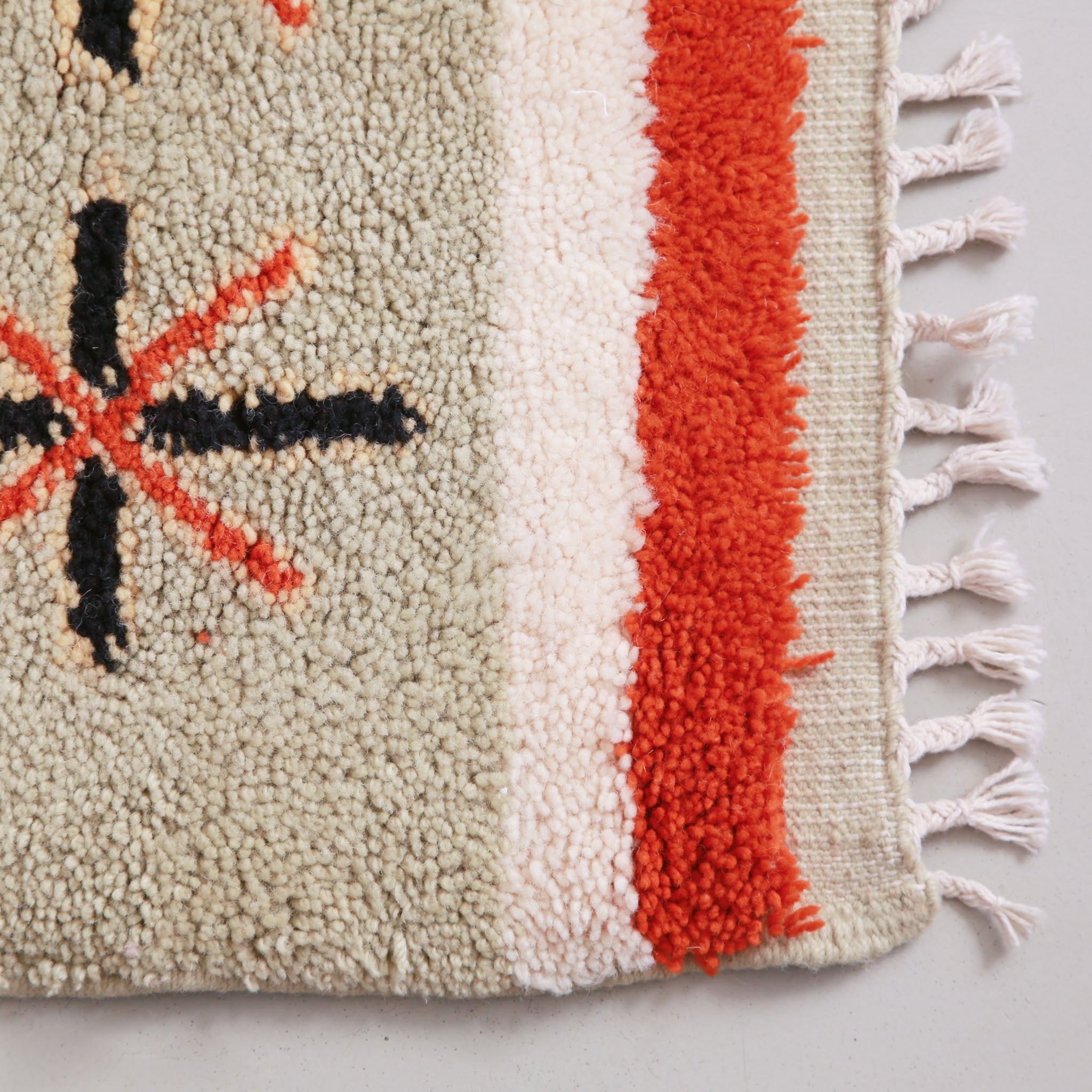 Angolo di un Tappeto marocchino fatto a mano con motivi geometrici in rosso, beige e crema, caratterizzato da strisce e simboli decorativi come croci e stelle