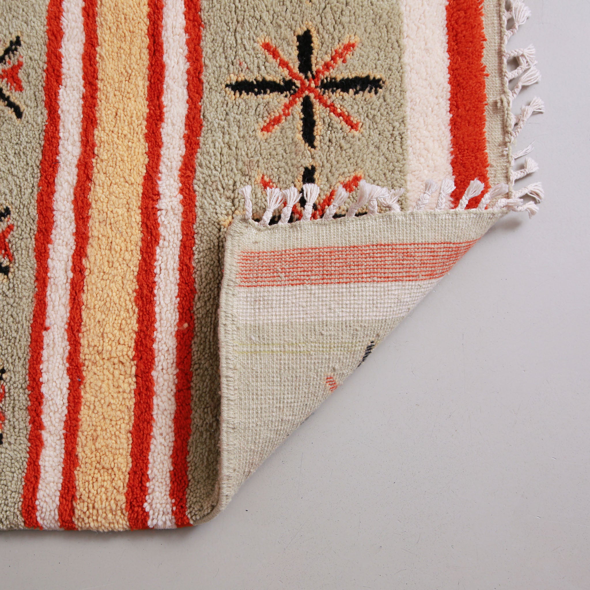 retro di un tappeto marocchino fatto a mano con motivi geometrici in rosso, beige e crema, caratterizzato da strisce e simboli decorativi come croci e stelle