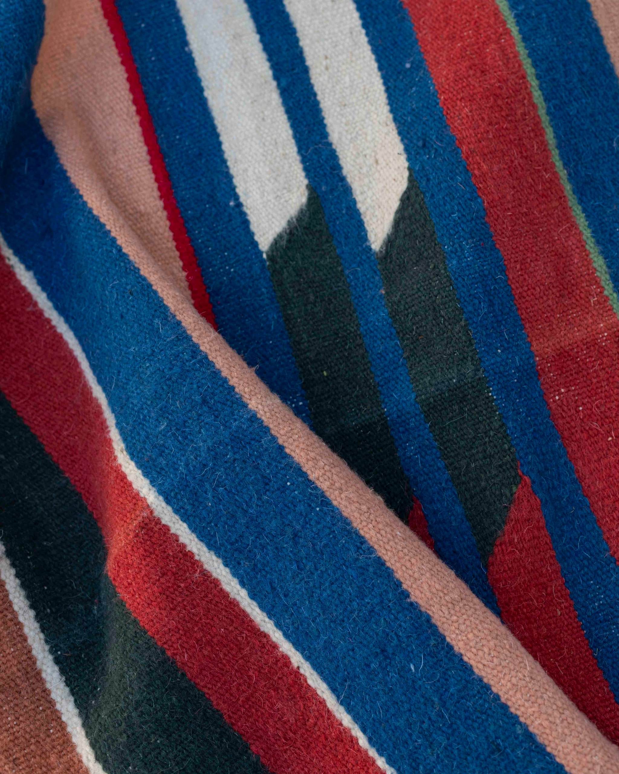 Texture ravvicinata del tappeto Hanbel a tessitura piatta con righe colorate e tasselli blu, verdi, rossi e bianchi