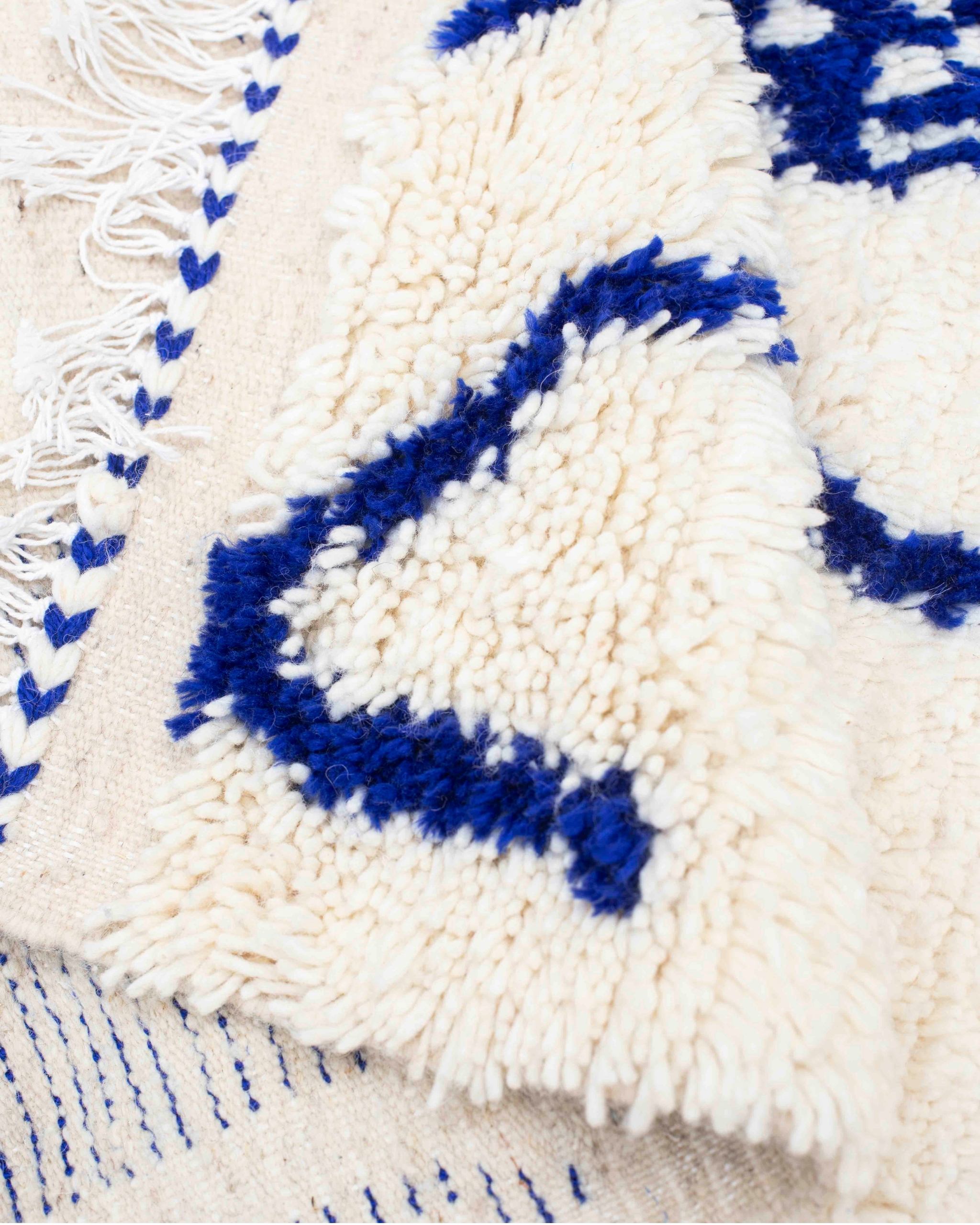 Texture ravvicinata della lana bianca e dei motivi blu del tappeto Azilal annodato a mano