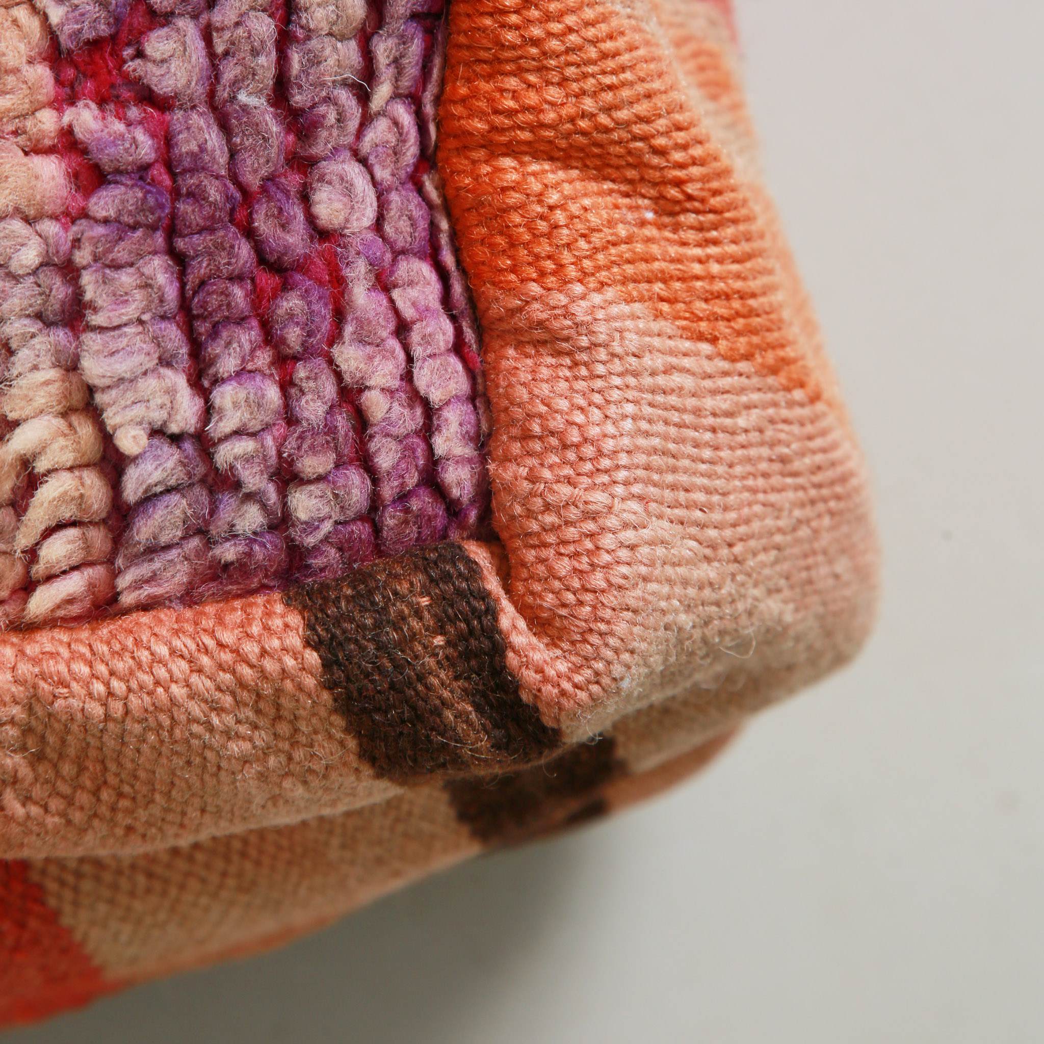 Texture dettagliata del pouf marocchino boucherouite con tecnica patchwork in tessuti riciclati, che mostra la combinazione di filati viola e corallo lavorati a mano