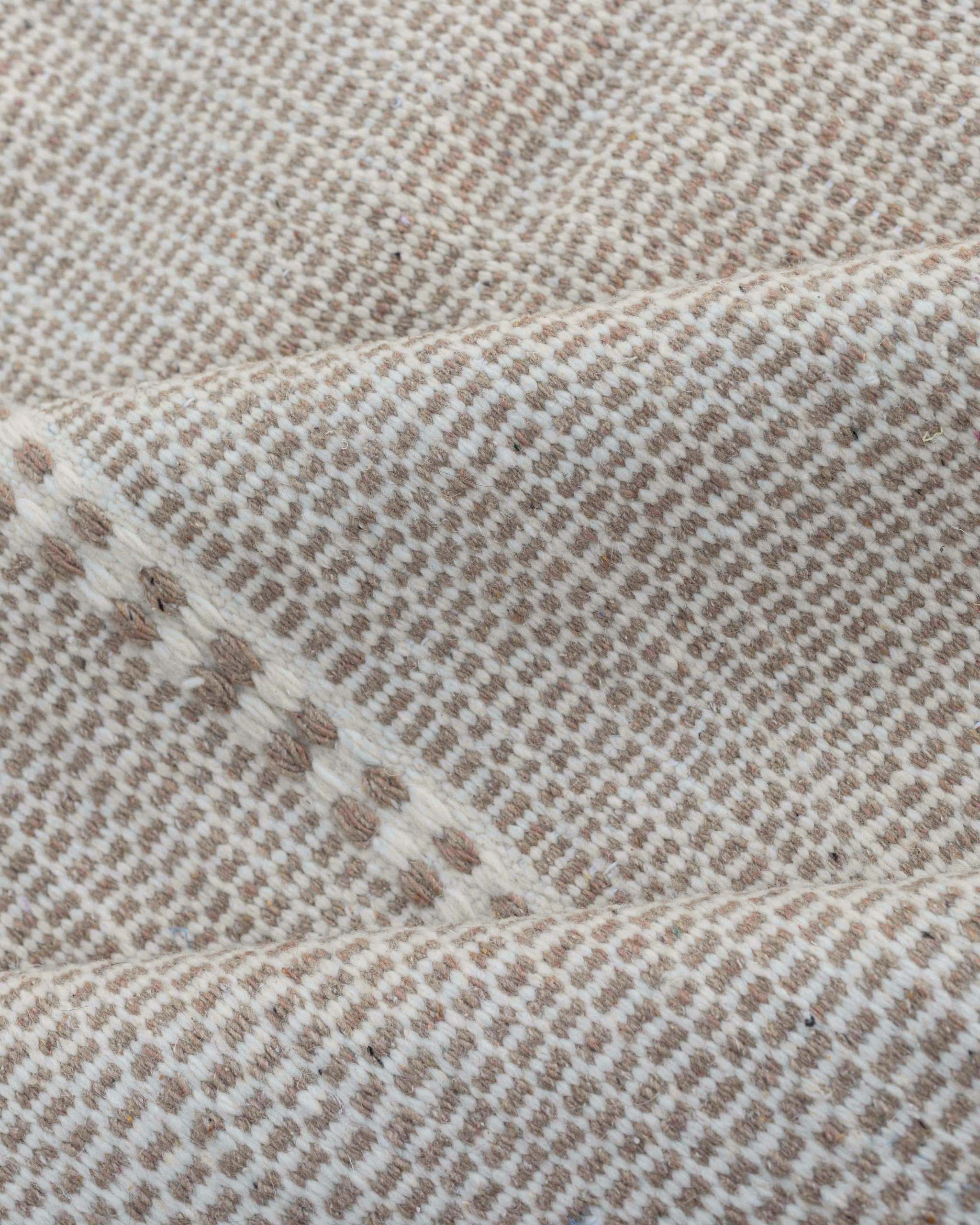 Dettaglio texture ravvicinata del tappeto Hanbel con alternanza di piccoli punti beige sabbia e bianco crema
