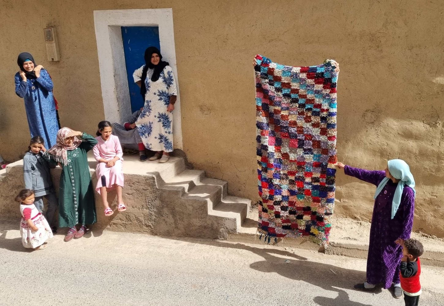 donne e bambini su una scala che guardano un tappeto steso dall'alto
