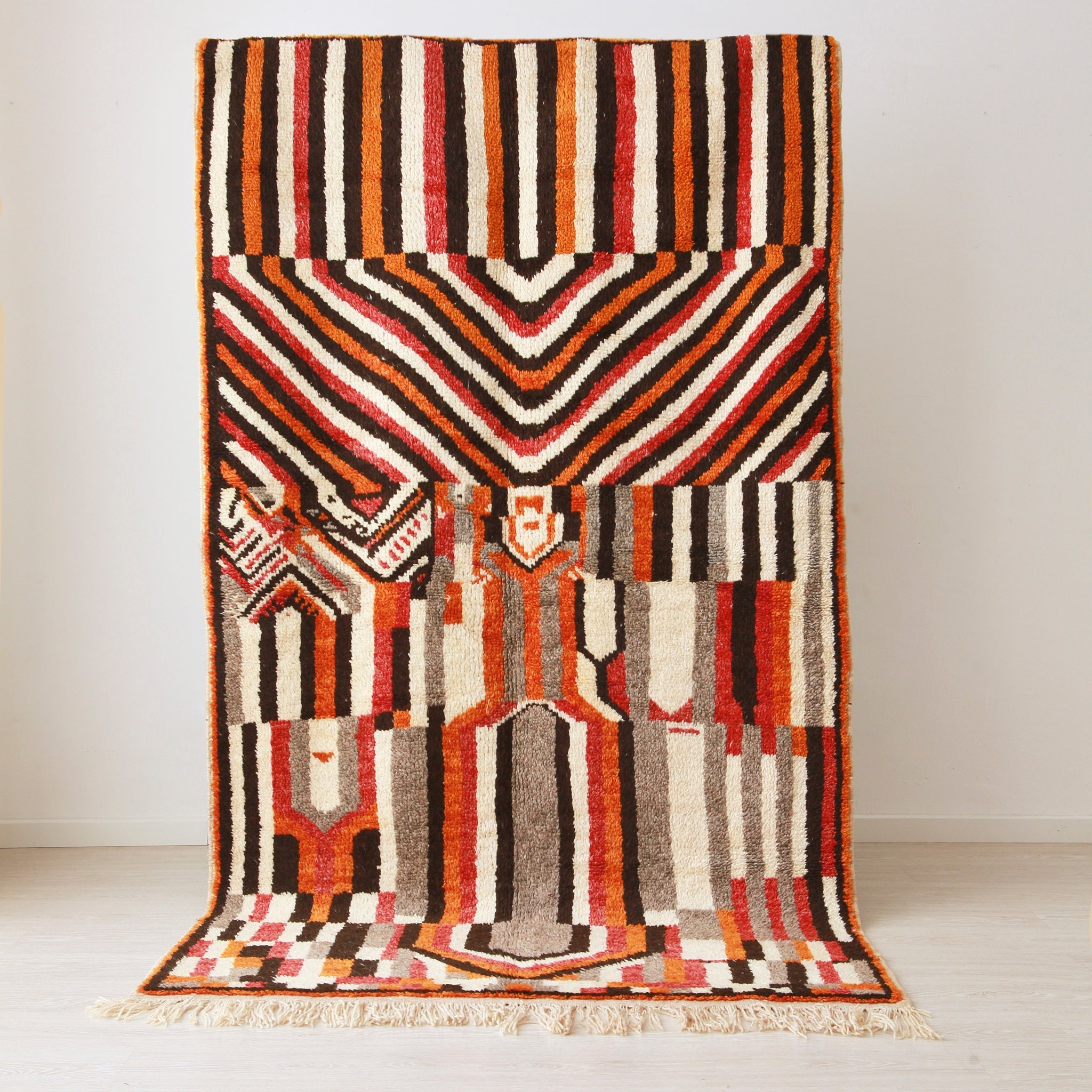 tappeto stile azilal con disegni geometrici che creano una fitta trama di forme dal colore nero, rosso, arancione bianco e grigio appeso