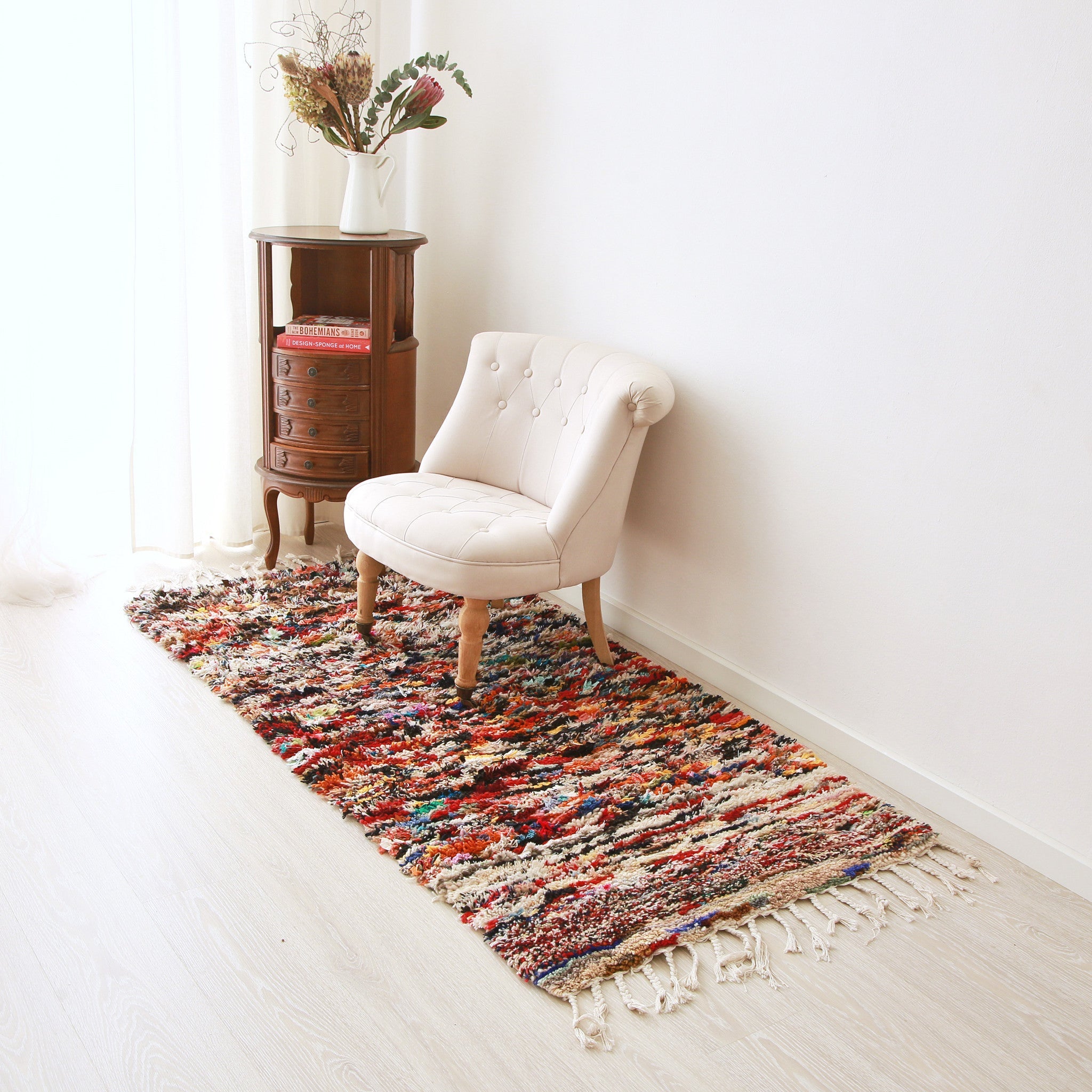 tappeto boucherouite realizzato con avanzi di tessuti e di filati di diversi colori sul pavimento con una poltrona bianca sopra