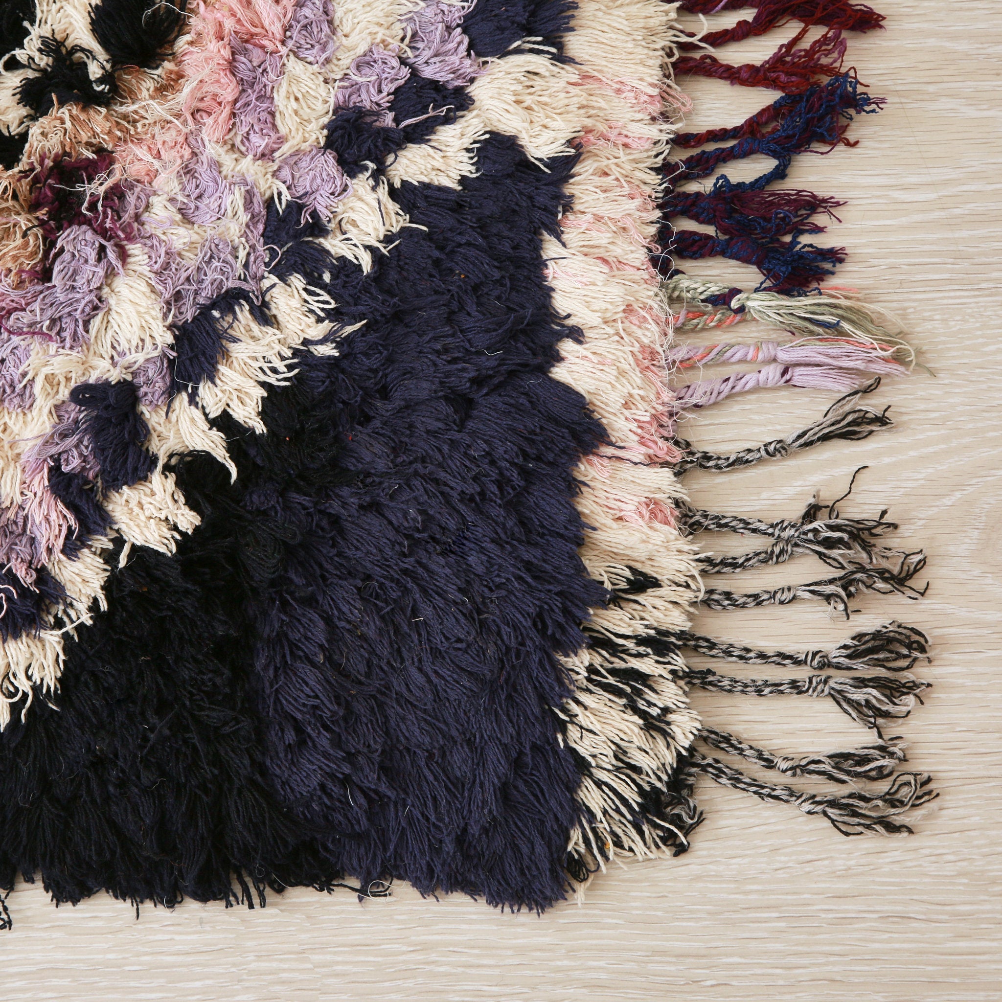 dettaglio di un angolo di un tappeto vintage realizzato con vilati dai colori blu scuro, rosa,lilla e bianco