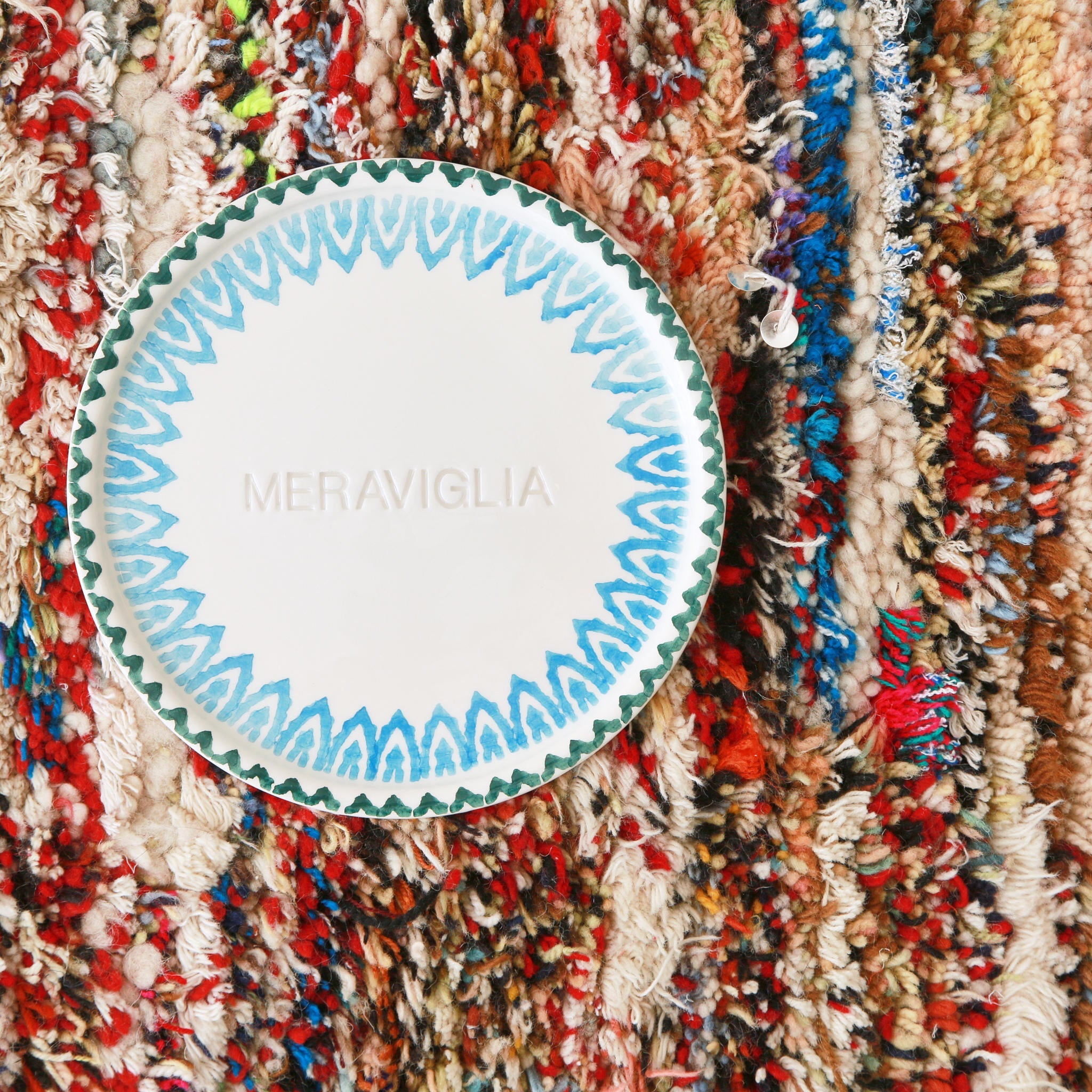 dettaglio di un piccolo tappeto marocchino realizzato con resti di lana e filati colorati con sopra un piatto bianco dove è scritta la parola meraviglia