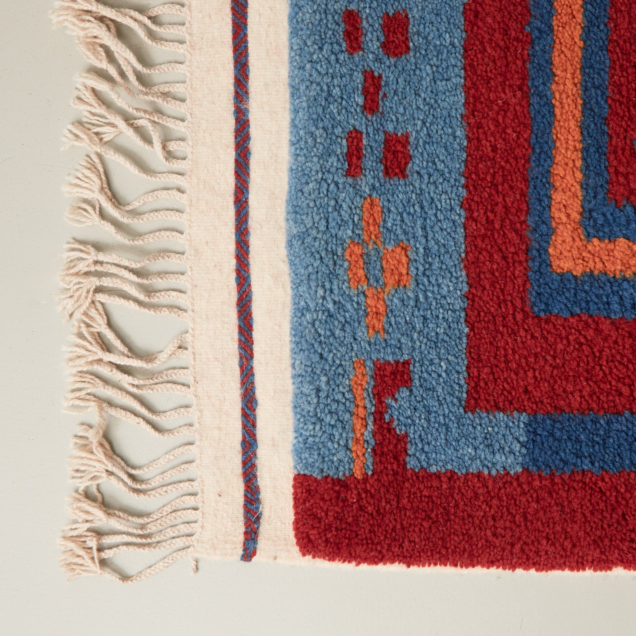 dettaglio della frangia rifinata con due diverse tecniche e del pelo corte e compatto di un tappeto taznakht piccolo realizzato con lana siroua tinta con colori naturali su base rossa e disegni geometrici