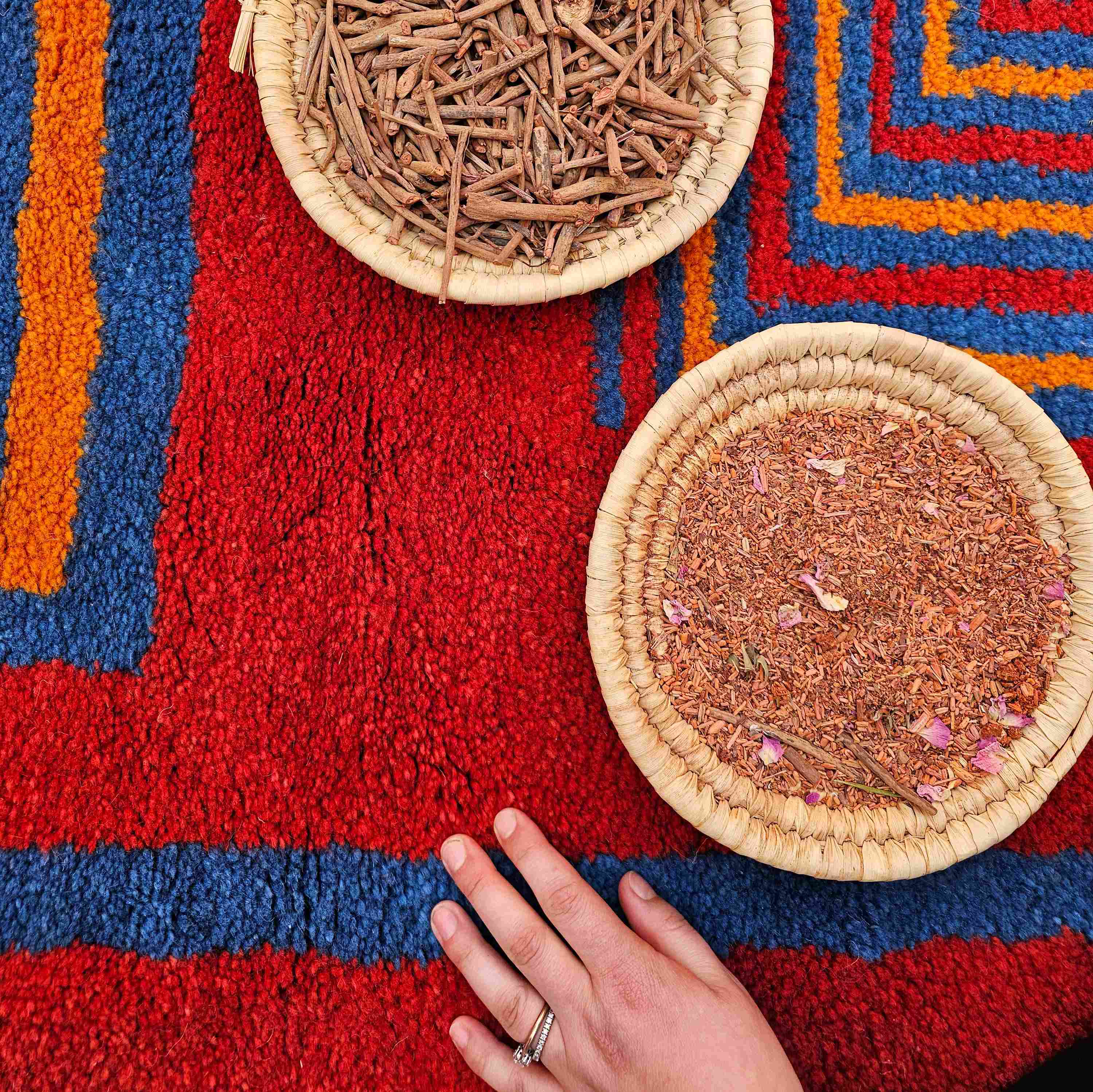 erbe tintorie in due cestini appoggiati su un tappeto con lana rossa tinta con metodi naturali e tradizionali