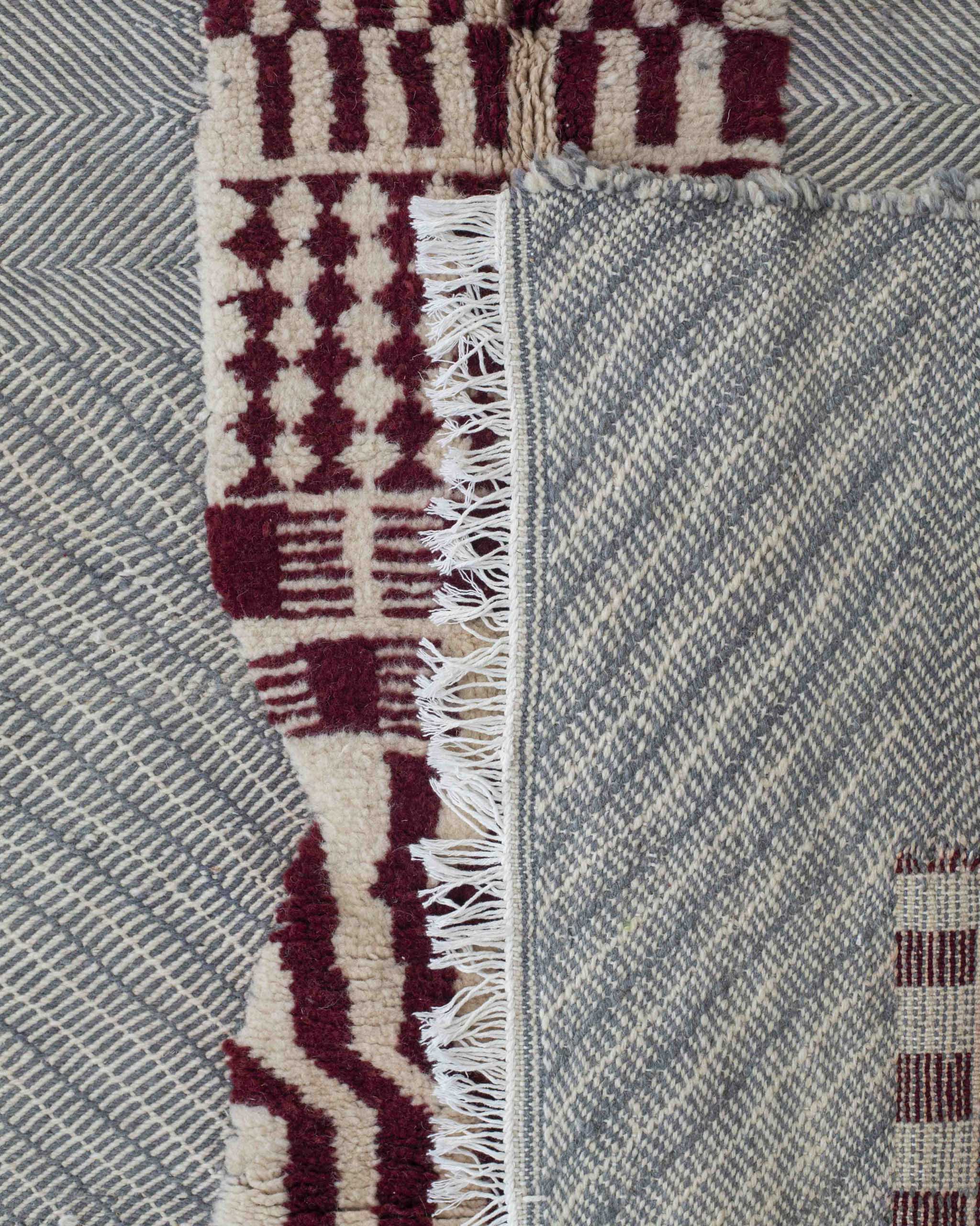Dettaglio del tappeto grigio-azzutto a righe e zigzag con sezioni in rilievo con decor geometrico bordeaux bianco