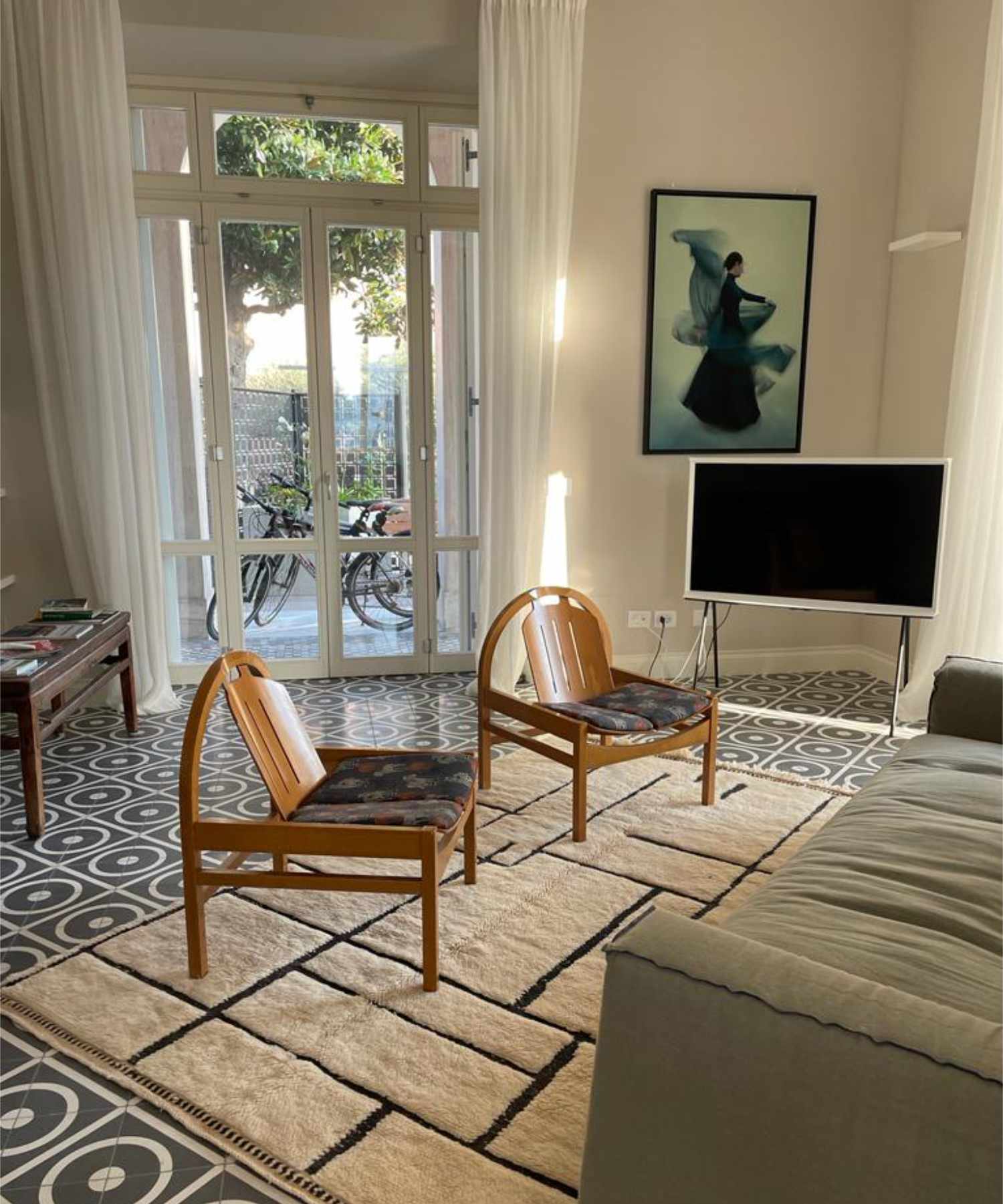 Beige Beni Mrirt Afara rug with black geometric pattern adorning a vintage, contemporary, industrial and mid-century modern living room, featuring vintage cement tiles and wooden chairs