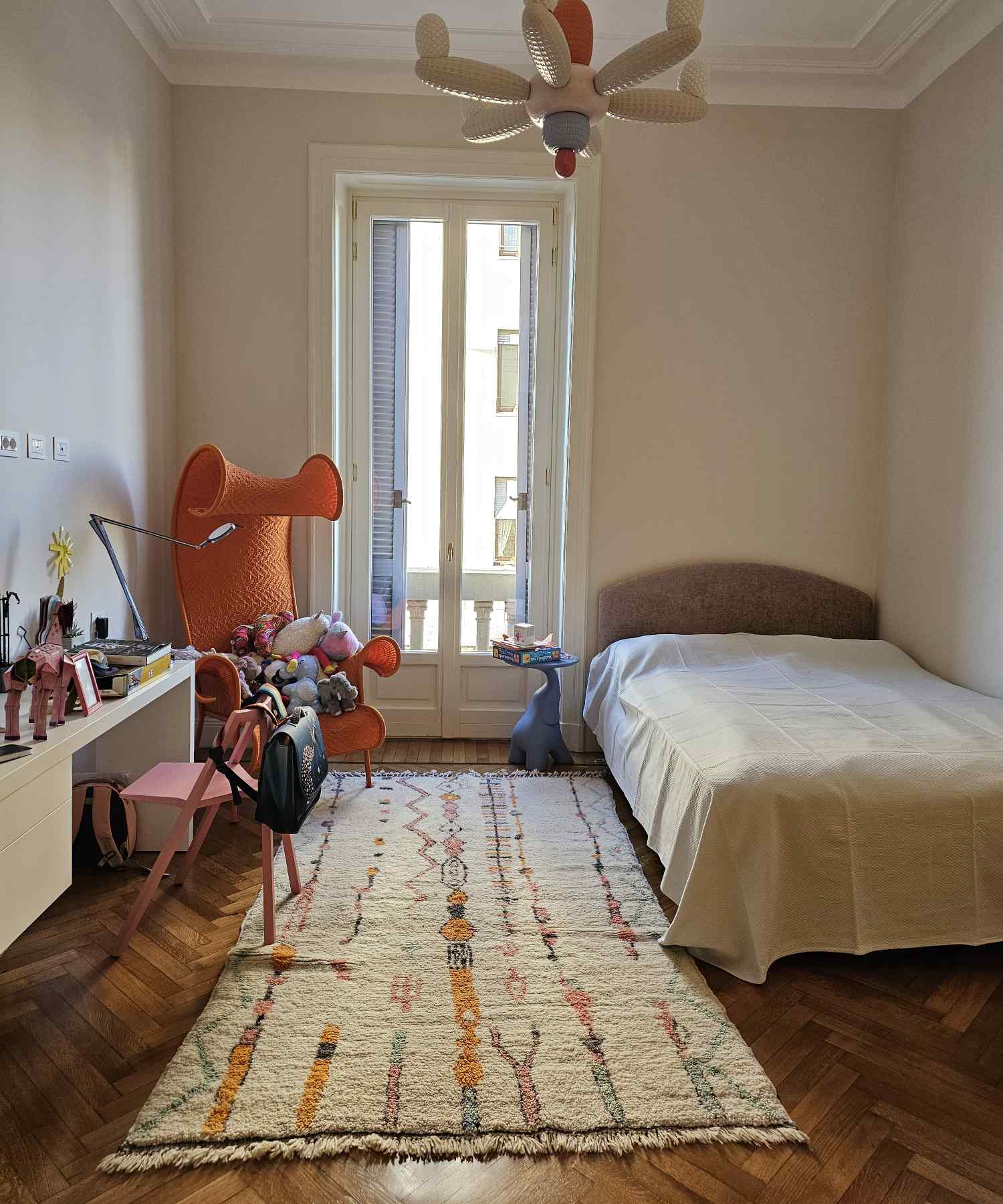 Tapis Azilal blanc avec motifs géométriques colorés qui décore une chambre d'enfant de style contemporain, moderne, éclectique et scandinave, avec chaise orange et parquet en chevron