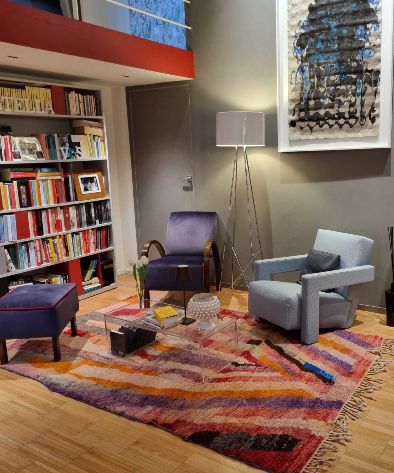 Tapis Boujaad multicolore avec motifs abstraits roses et violets qui décore un salon-bibliothèque de style contemporain, éclectique, artistique et mid-century modern, avec fauteuils vintage et bibliothèque