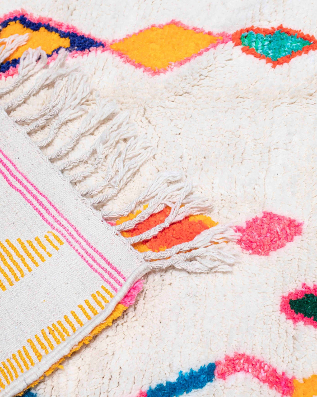 Dettaglio delle frange e del bordo colorato rosa e giallo del tappeto Azilal con rombi multicolor