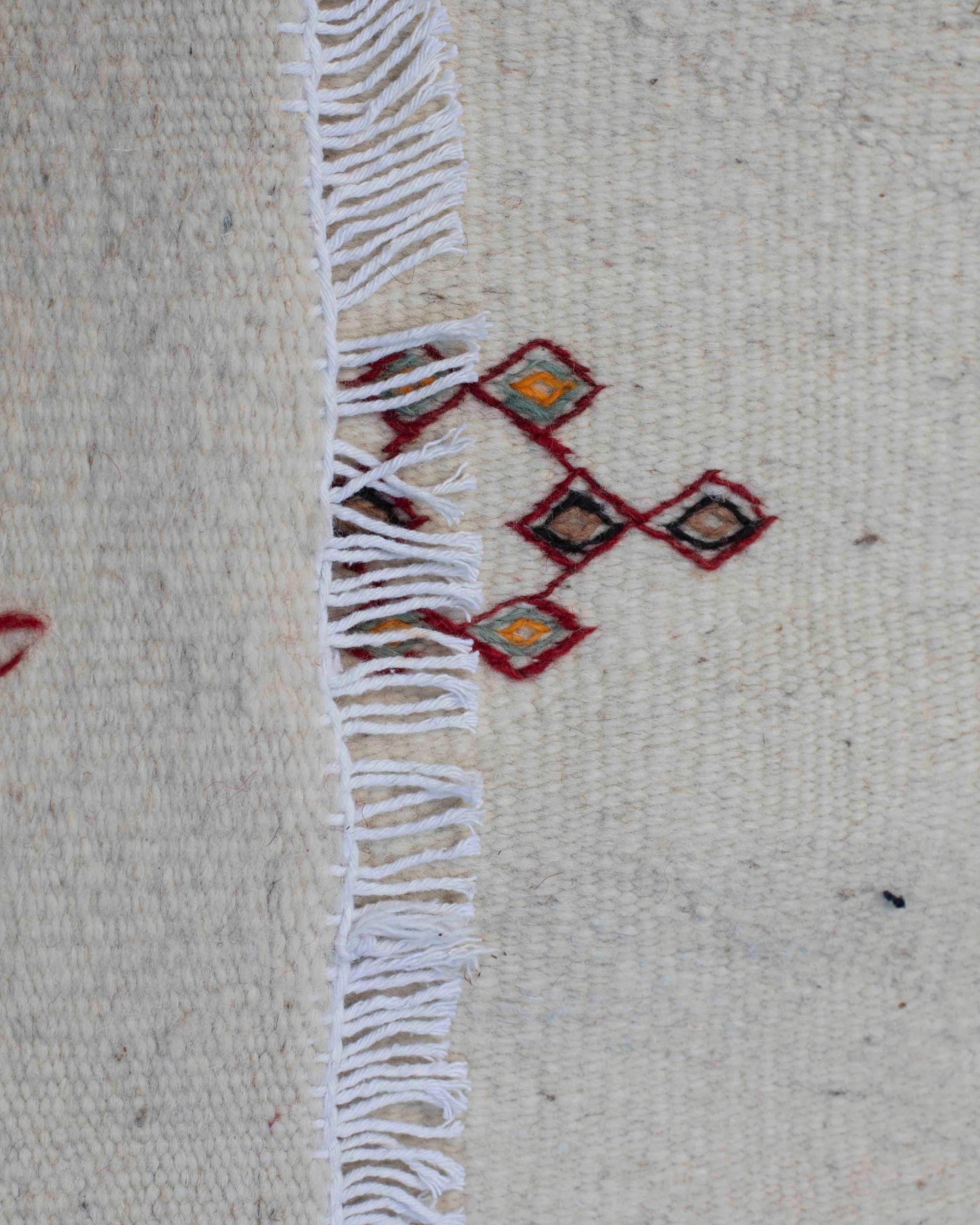 Dettaglio ricamo a rombi e frange sul tappeto kilim in lana écru a tessitura piatta