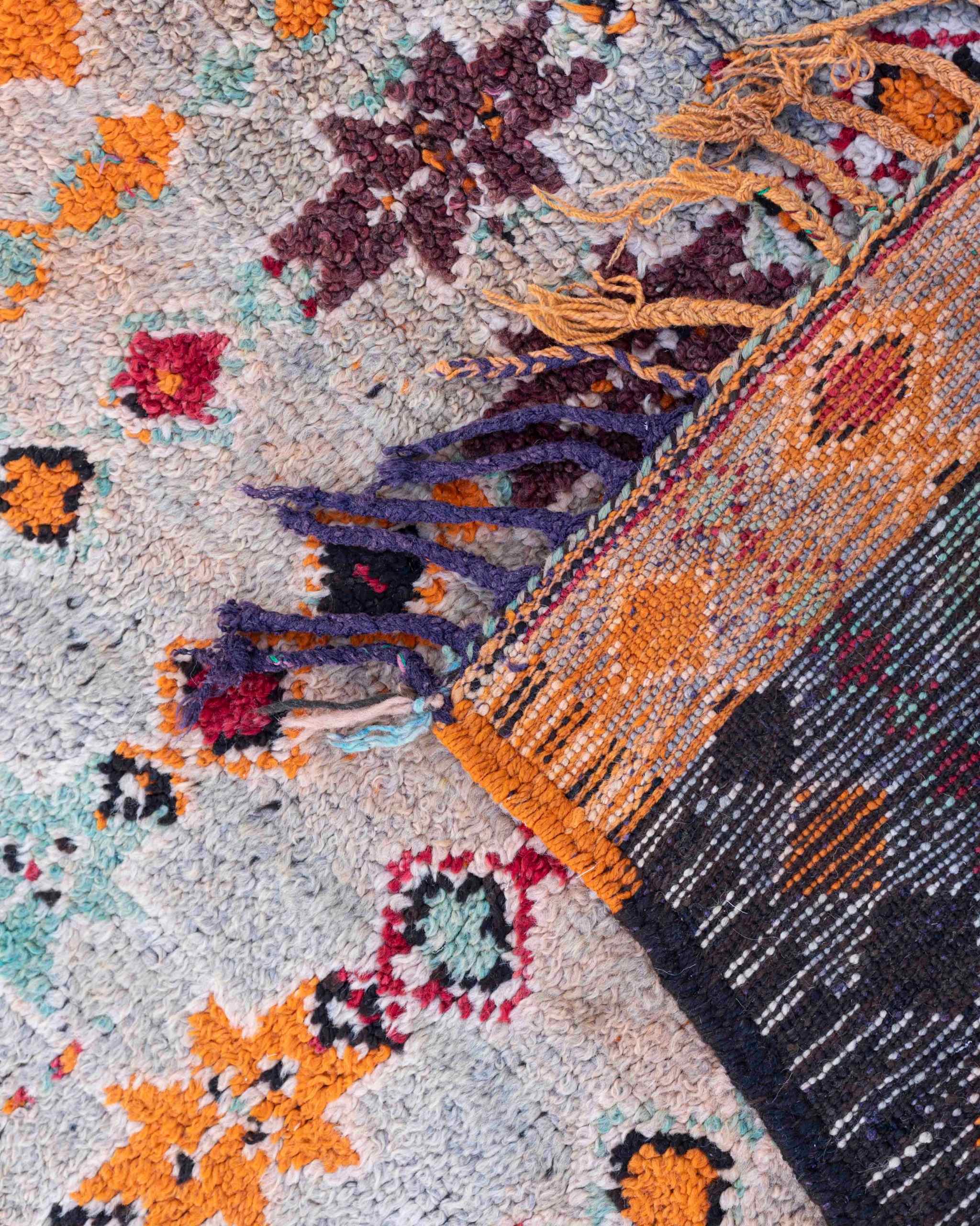 Dettaglio del retro e delle frange della passatoia Taznakht vintage in lana con motivi geometrici arancioni, rossi, azzurri e prugna