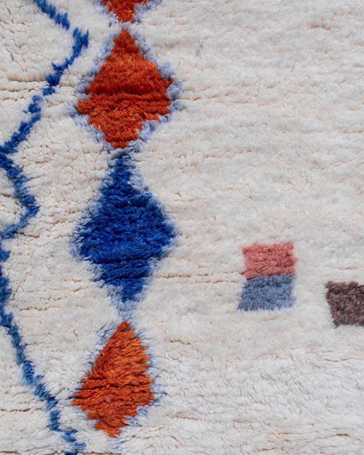 Dettaglio dei rombi blu e terracotta e dei segni colorati su lana bianca del tappeto Azilal