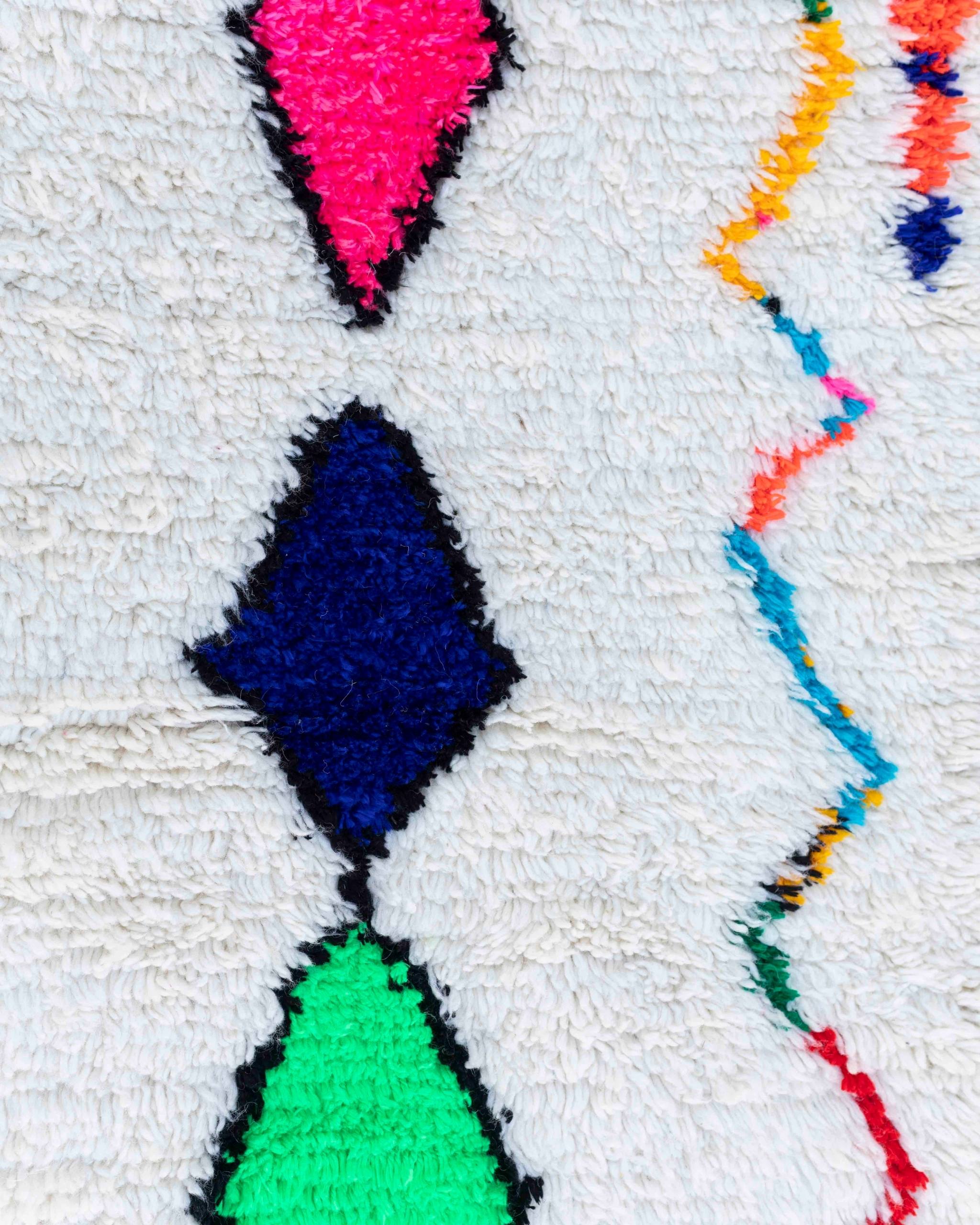 Dettaglio dei rombi colorati e delle linee zigzag blu, verde e rosa fluo sul fondo bianco avorio del tappeto Azilal