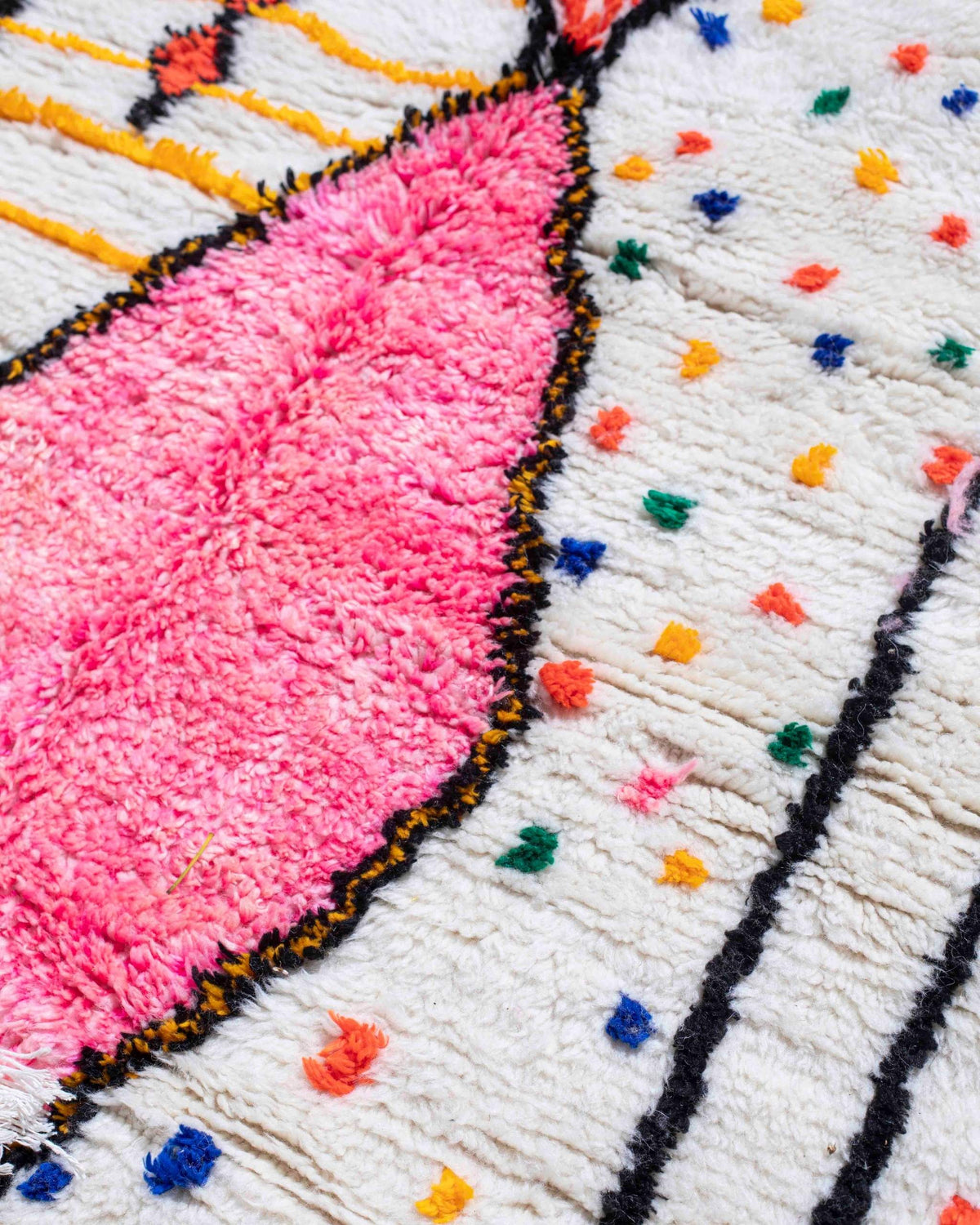 Texture ravvicinata del tappeto berbero bianco con piccoli pois tipo coriandoli colorati e grande rombo rosa