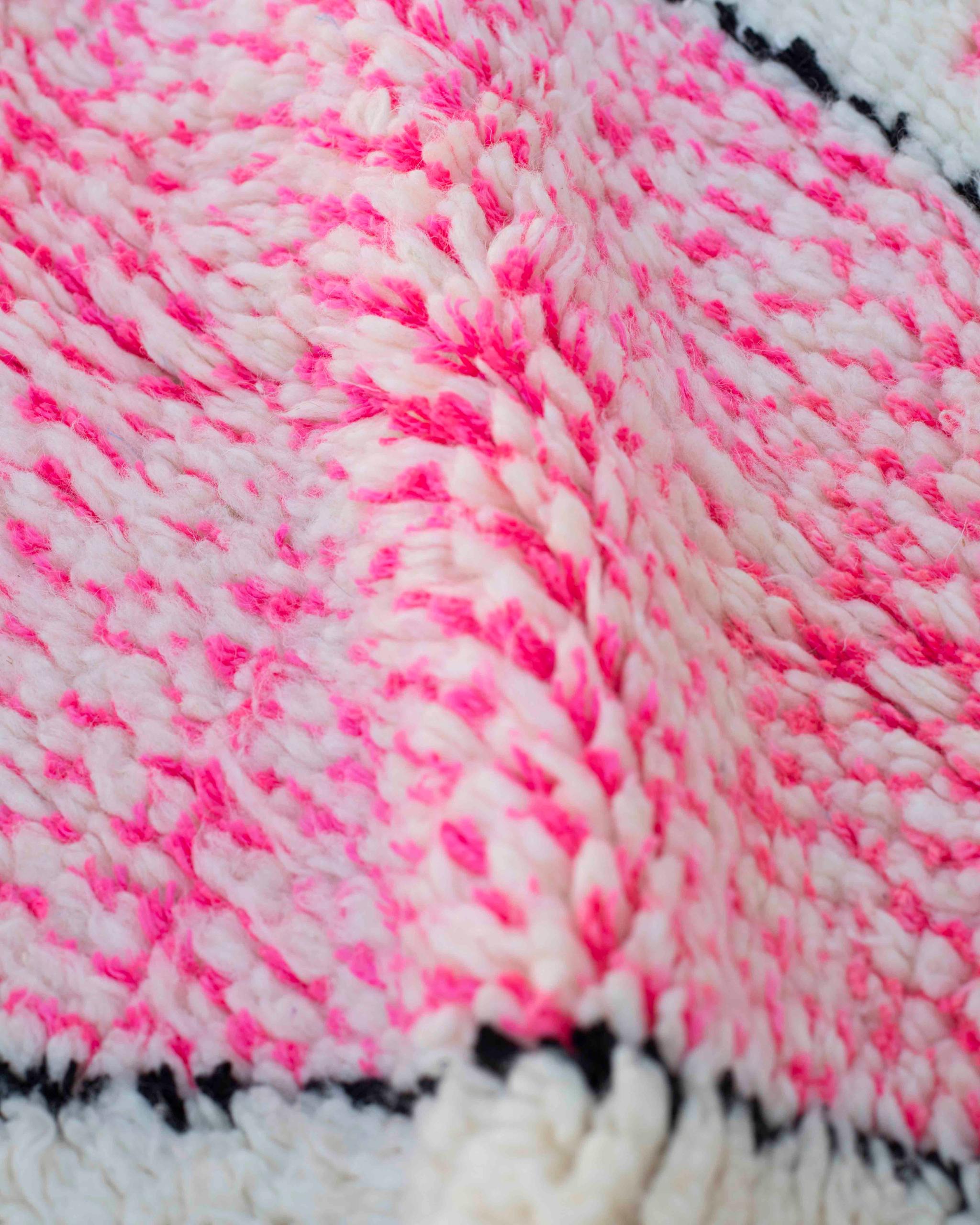 Dettaglio del tappeto in lana bianca con disegno rosa fluo bordato di nero 