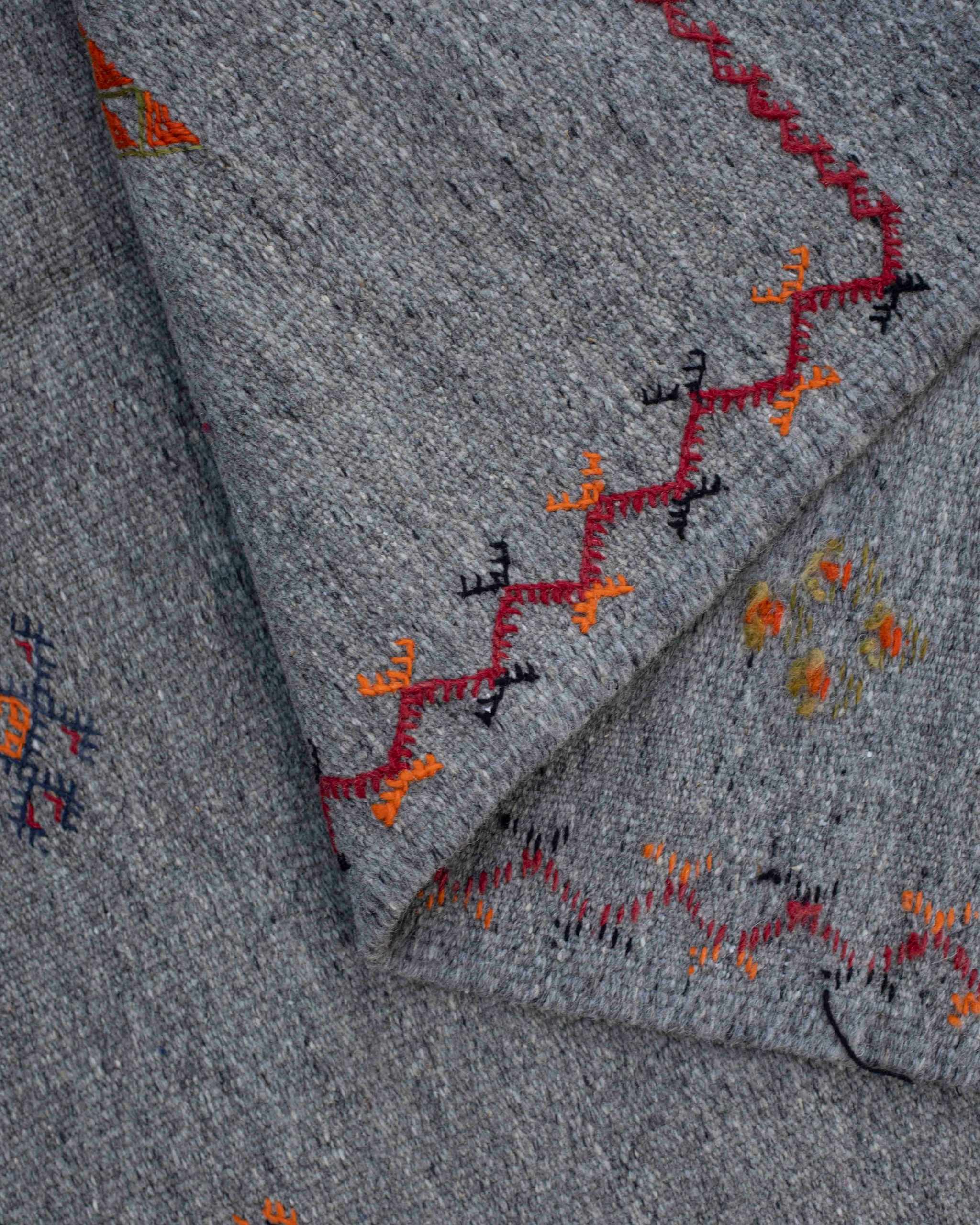 Particolare del tappeto kilim Akhnif grigio con ricami berberi geometrici, bordo zigzag in rosso, arancione, nero, blu
