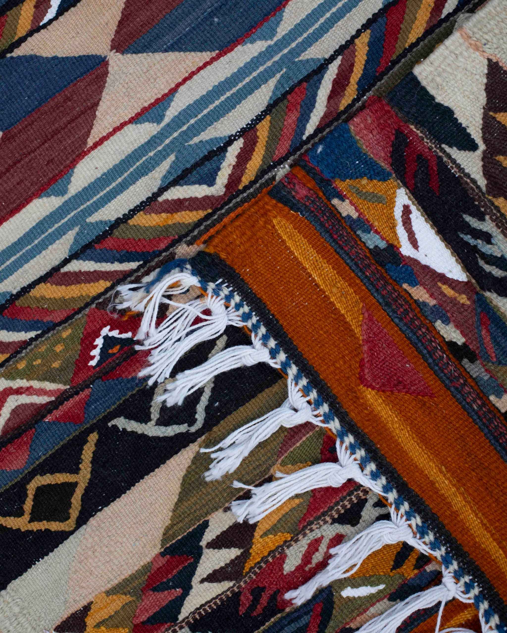 Dettaglio del piccolo tappeto Kharita kilim marocchino in lana con frange e pattern geometrico multicolore a rombi, triangoli e righe