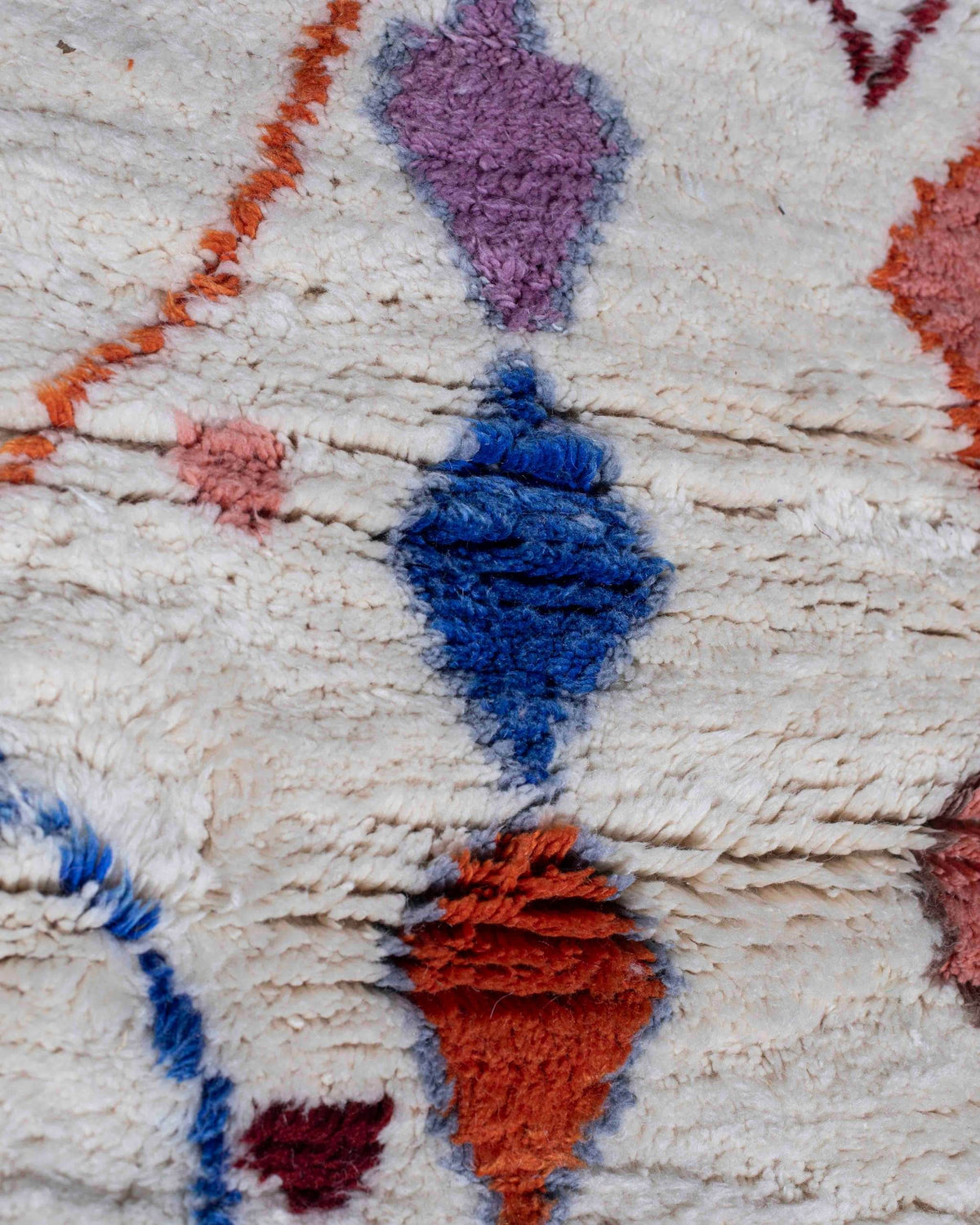 Dettaglio del tappeto a losanghe e segni grafici blu, lilla e terracotta del tappeto berbero Azilal in lana