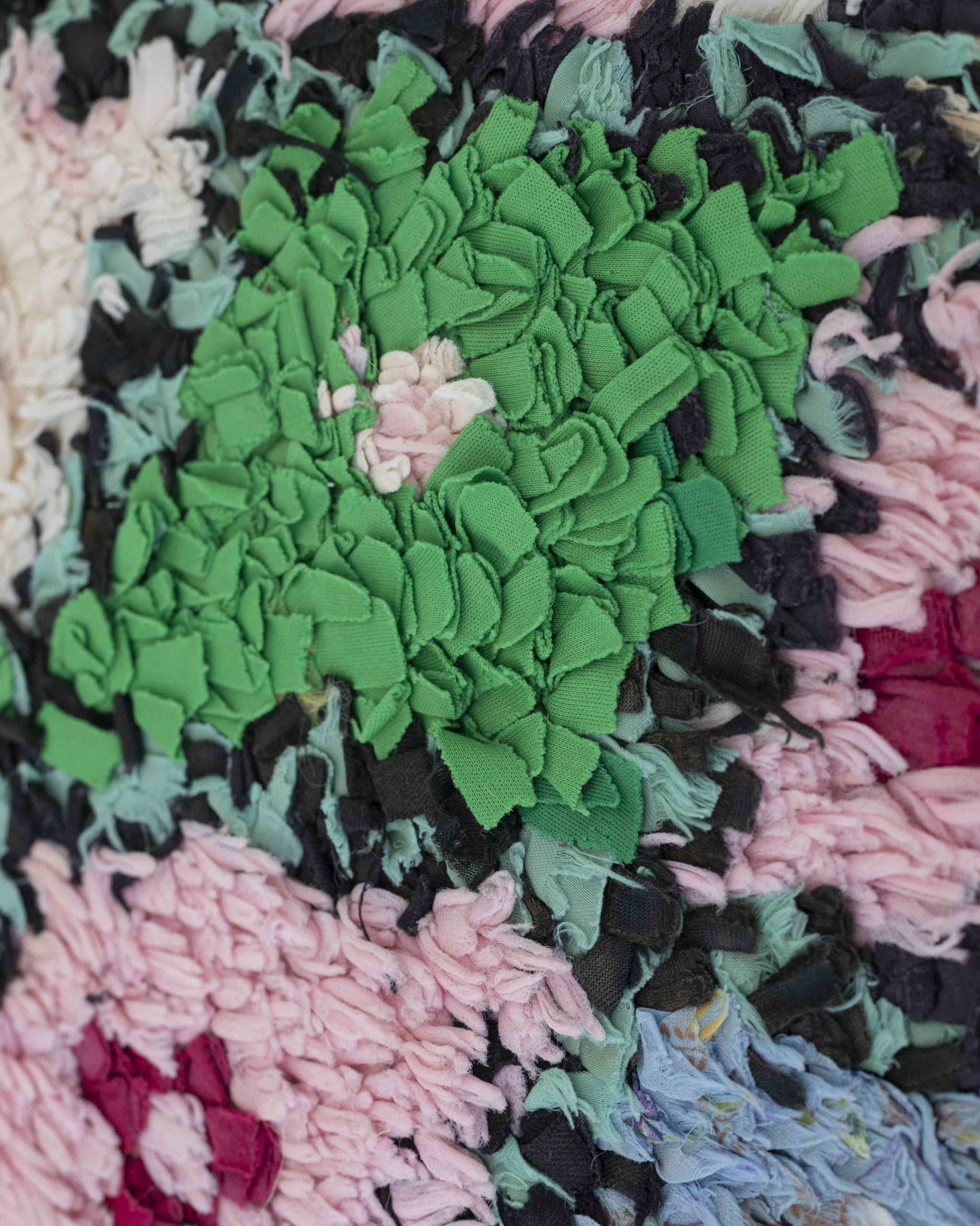 Dettaglio della superficie del tappeto a striscette di stoffe riciclate rosa, verdi, nere,azzurre, rosse