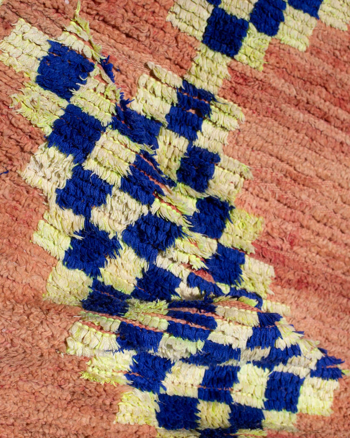 Dettaglio del tappeto vintage in lana a pelo corto arancione con scacchi blu e giallo-verdi ripiegato per mostrare la struttura annodata