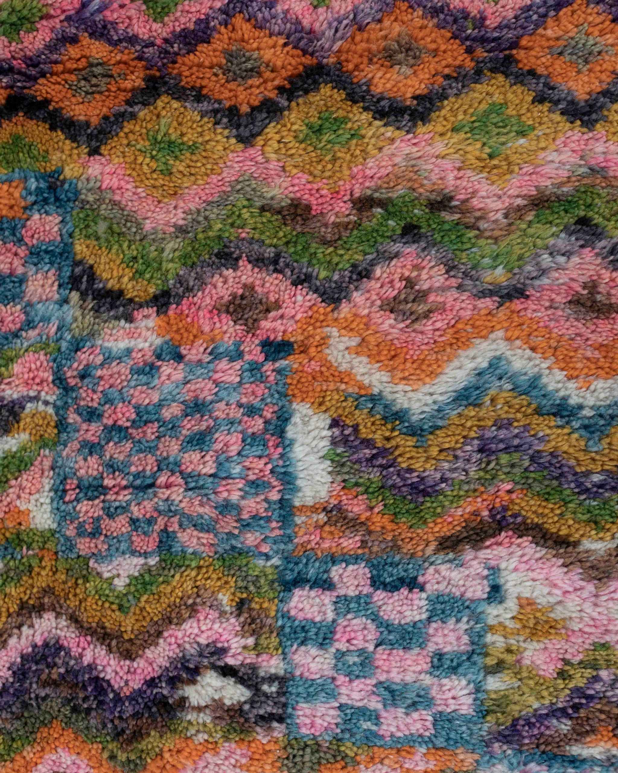 Dettaglio del tappeto in lana multicolore con fantasia a rombi, zigzag e quadri a scacchi nei colori rosa, verde, arancione, azzurro,bianco