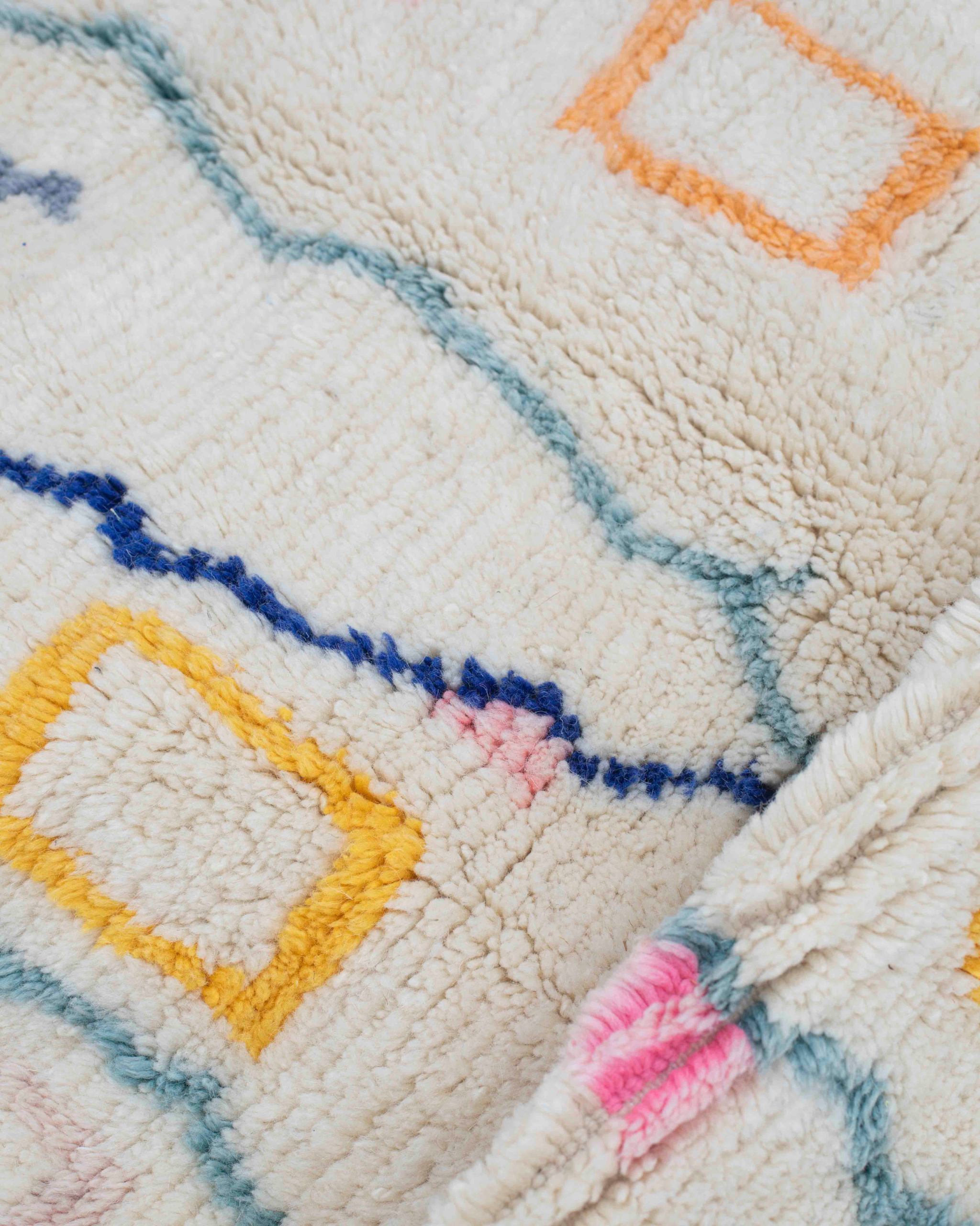 Dettaglio delle linee zigzag blu, turchesi e dei piccoli motivi gialli, arancioni e rosa sul tappeto berbero in lana bianca
