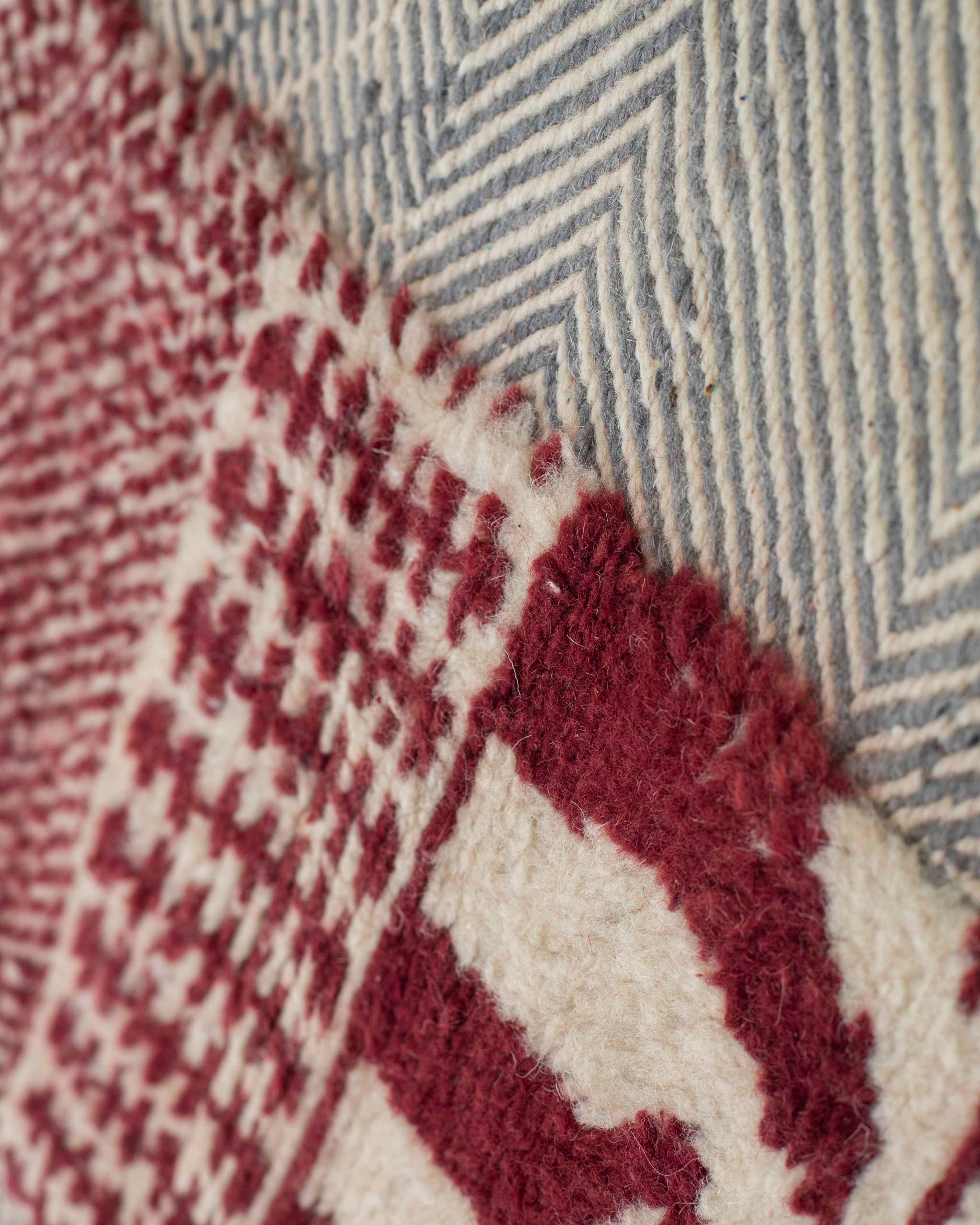 Dettaglio dei due tipi di tessitura del tappeto con sezioni piatte grigio-azzurre e sezioni a pelo corto rosse e bianche
