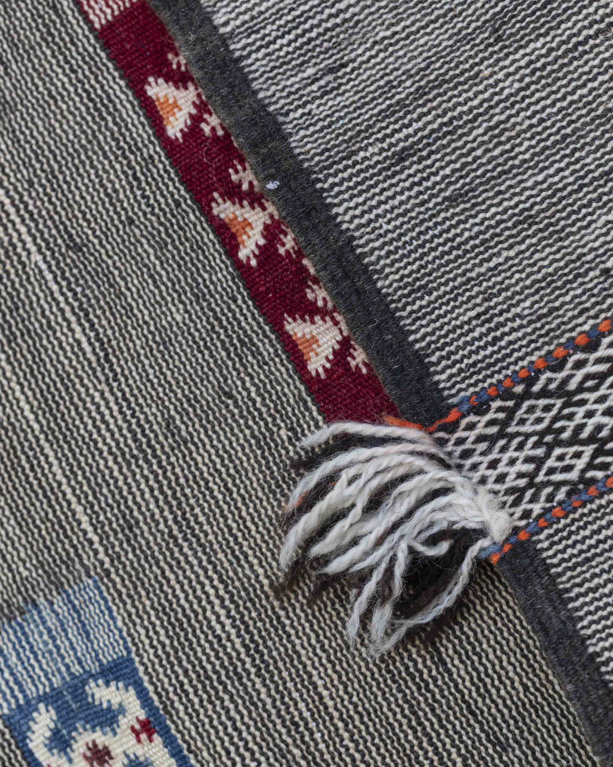 Dettaglio del tappeto kilim a righe sottilissime bianche e nere con inserti colorati e frange sparse