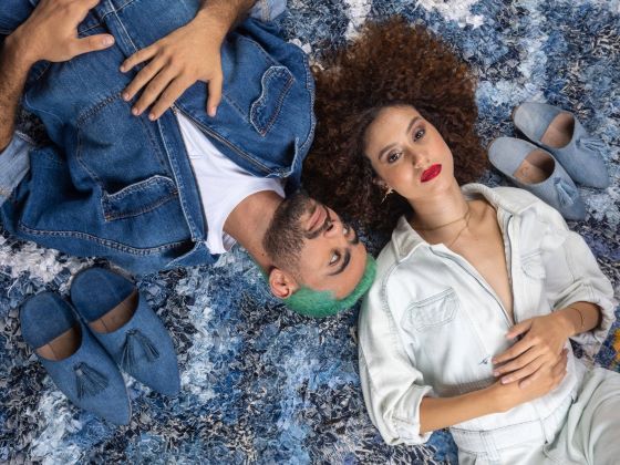 Collection Casa Denim: modèles allongés sur un tapis boucherouite marocain avec des babouches artisanales en jean recyclé. La composition artistique illustre la fusion entre l'artisanat traditionnel marocain et le denim durable.