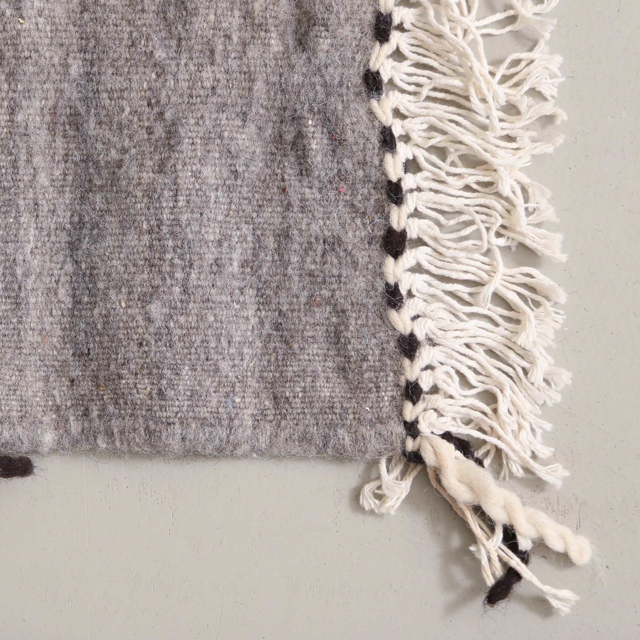 angolo di un tappeto a tessitura piatta realizzato a mano con lana grigia