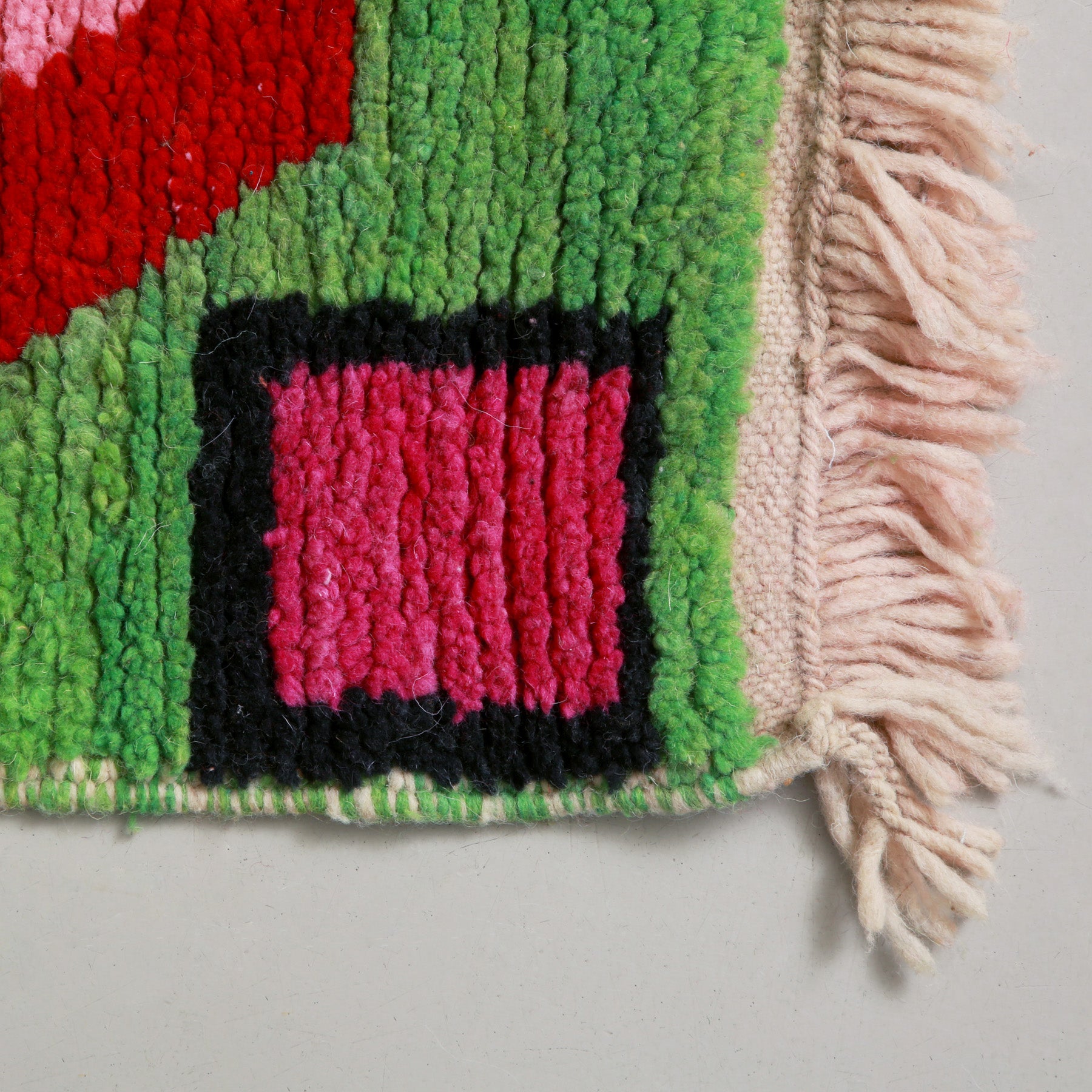 angolo di un tappeto con lana veder e grande quadrato fucsia con bordo nero. la frangia e in lana bianca