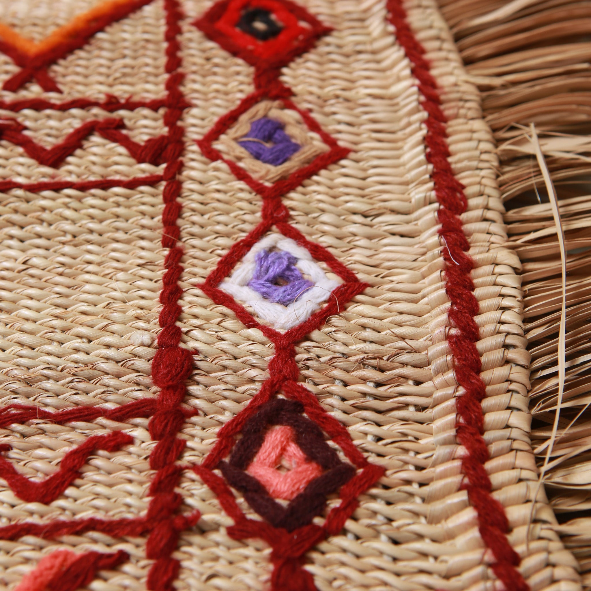 Rombi colorati in viola, arancione e rosa ricamati su stuoia hassira marocchina, dettaglio dei motivi geometrici tradizionali e della frange in paglia naturale, simboli amazigh berberi autentici