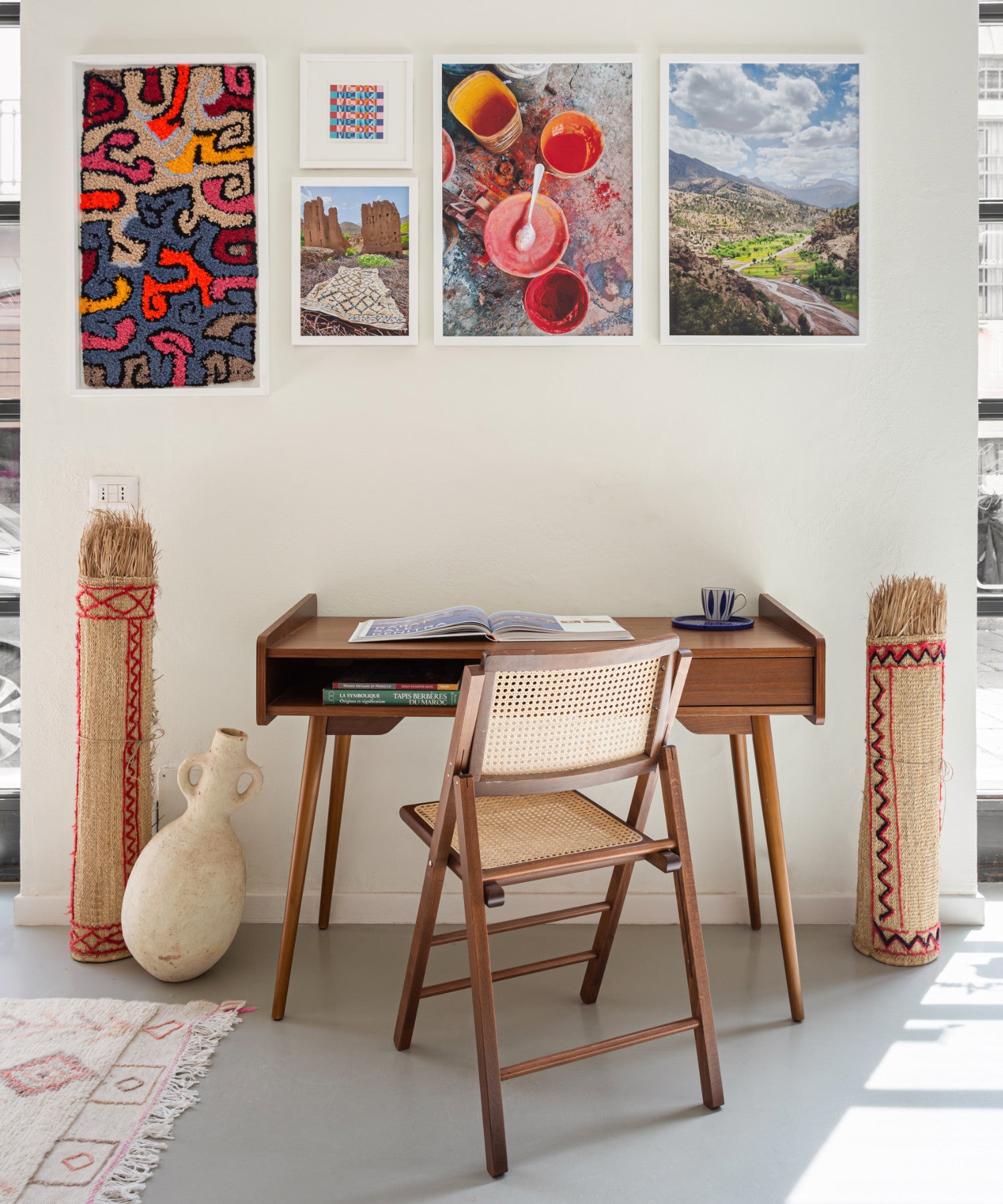 gallery wall con tre foto una stampa e uno tappeto appesi e sotto un tavolino in legno marrone. ai fianchi del tavolo delle stuoie in paglia arrotolate