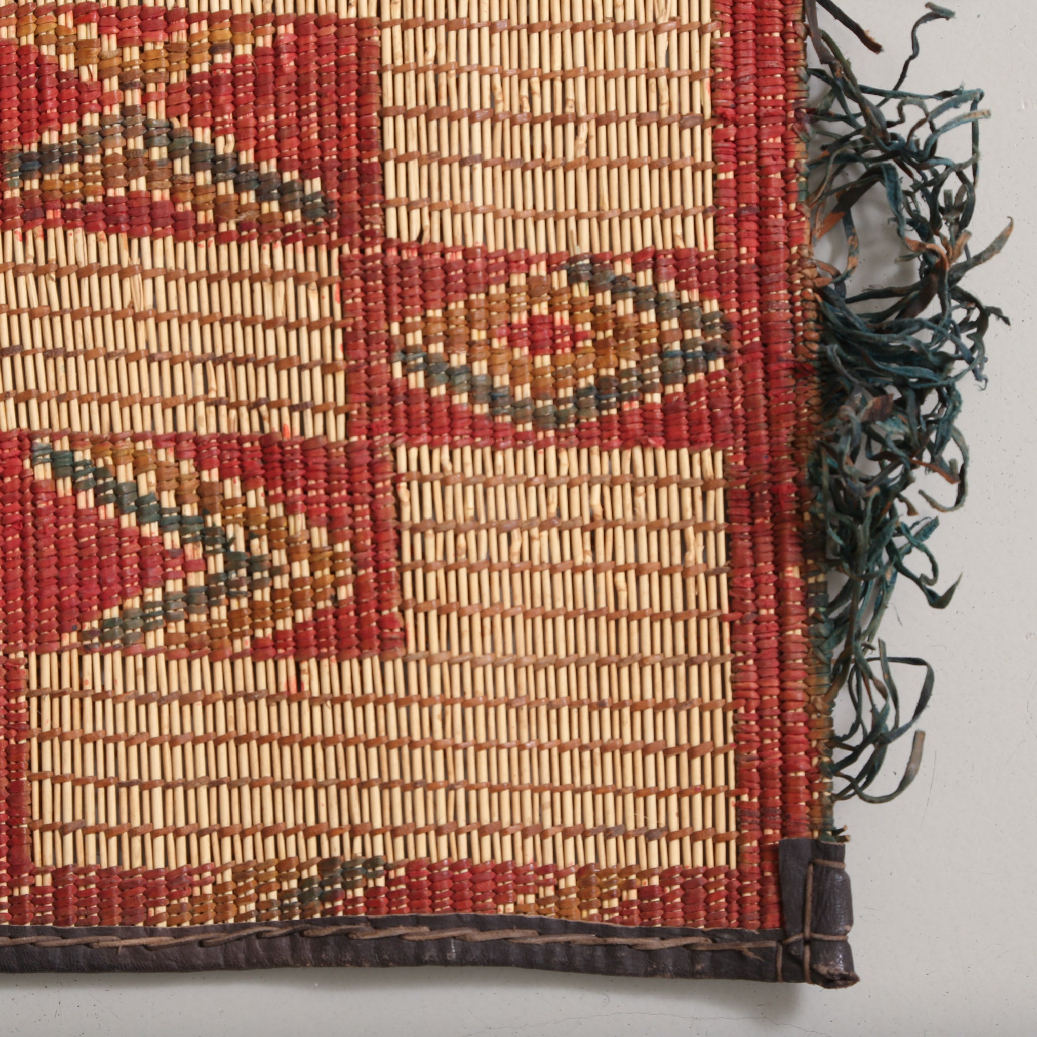 angolo di una stuoia tuareg con fili di cuoio colorati intrecciati lungo il bordo di color rosso