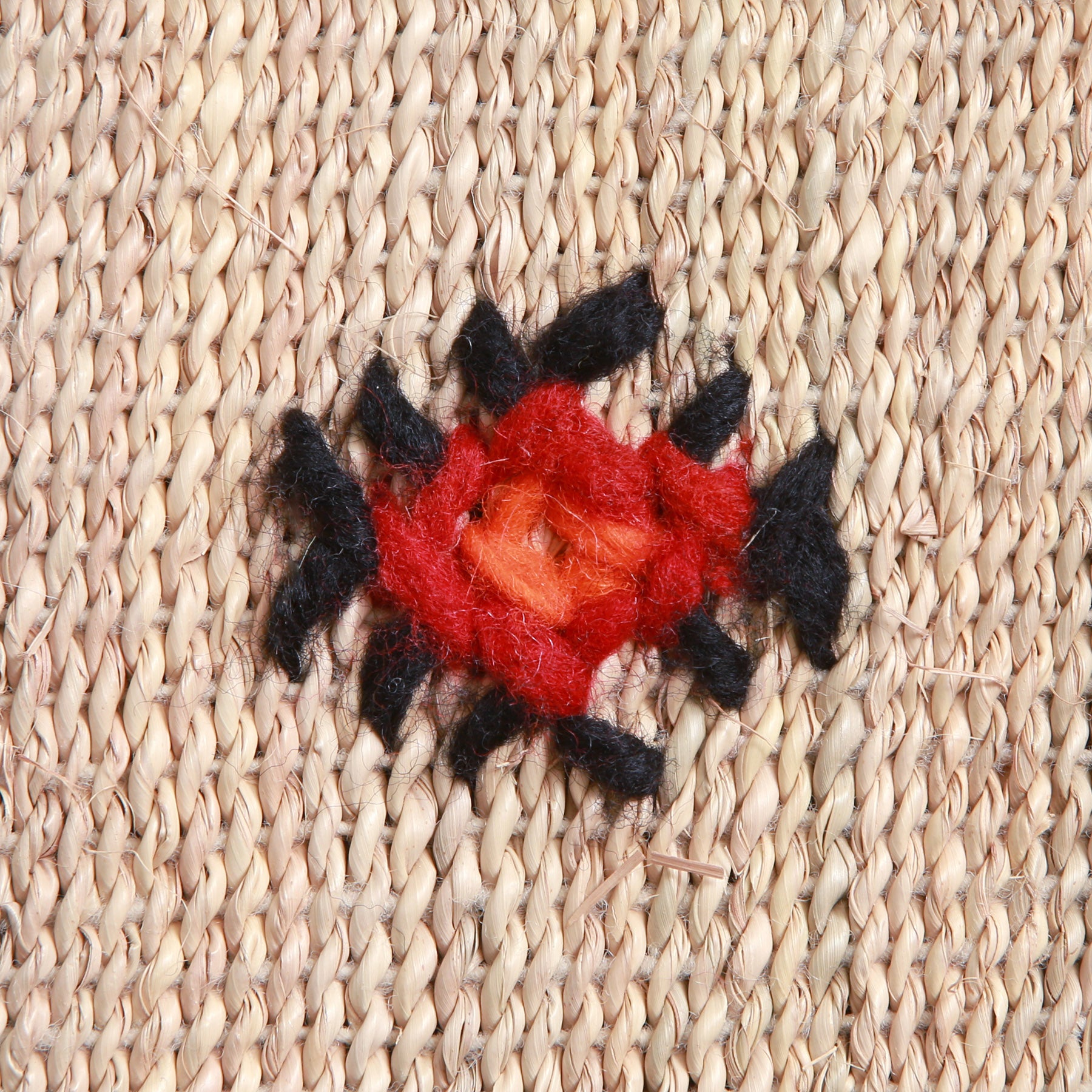dettaglio di un ricamo amazigh in lana nera rossa e arancione presente su una stuoia in paglia di palma